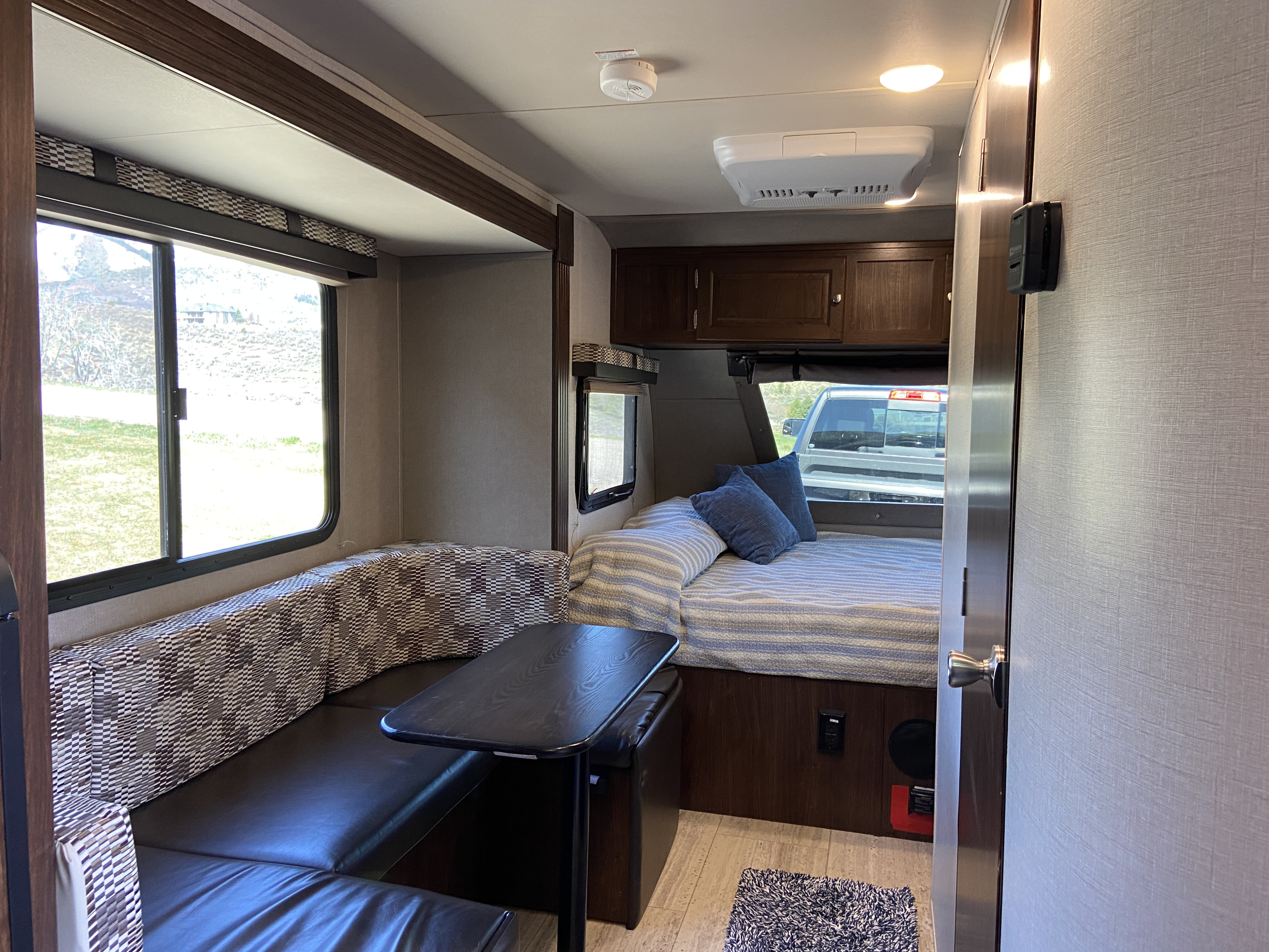 Interior of an RV rental showing the dinette with U-shaped seating, a cozy bed, and overhead cabinets. Ideal for travel adventures.. Forest River Palomino Palomini 2018