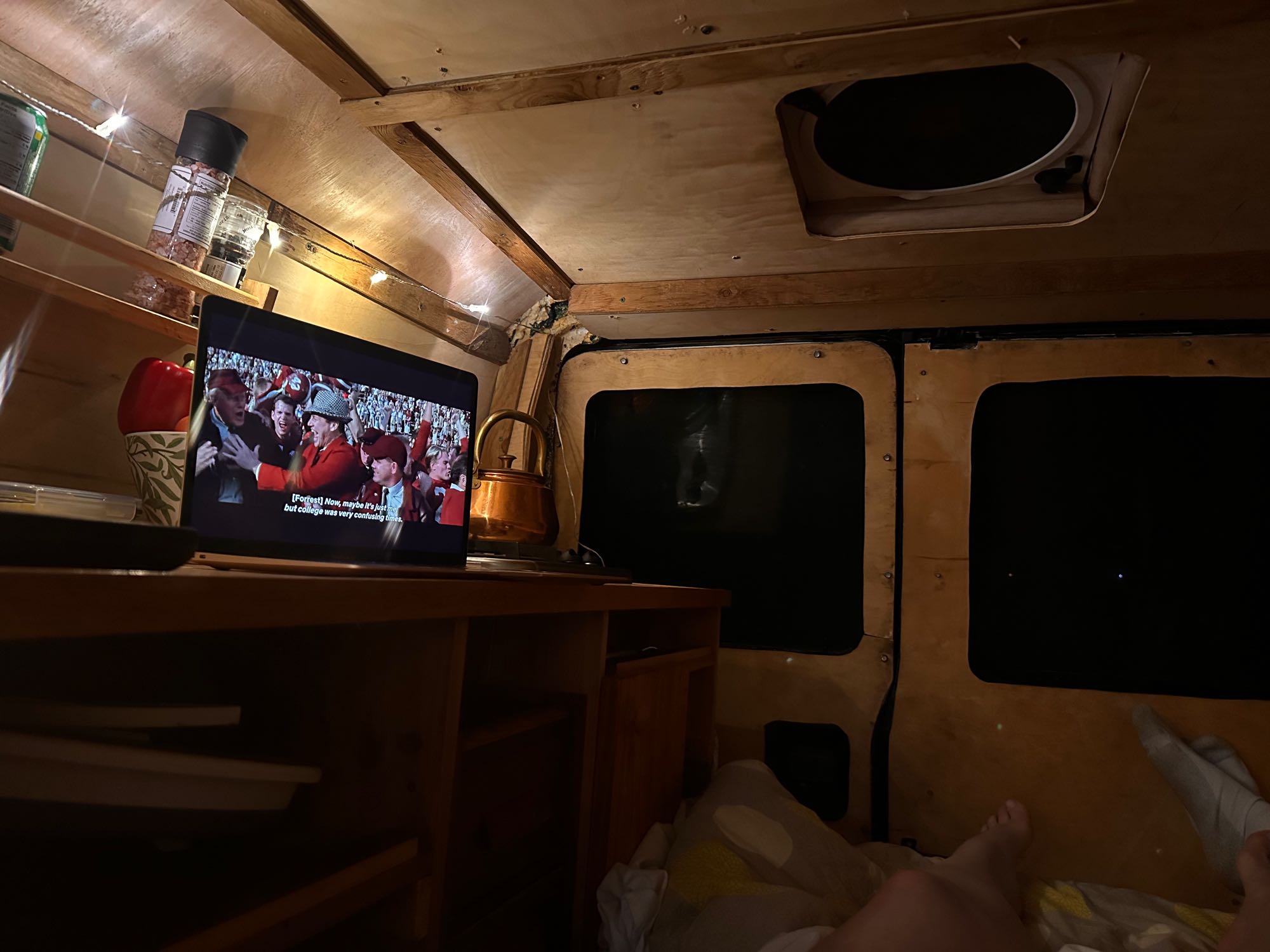 Cozy RV rental interior at night. Watch a movie on a laptop amidst wooden panels & string lights, experiencing van life.. Ford Econoline 150 2007
