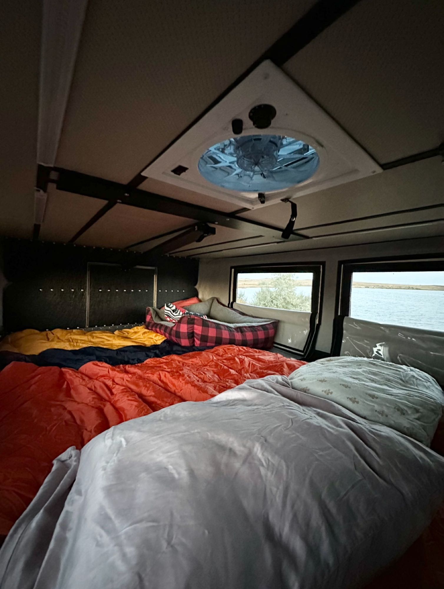 Cozy RV rental interior with multiple beds, a roof vent, and scenic lake views from the windows. Perfect for camping adventures.. Four Wheel Campers Shell Models 2020
