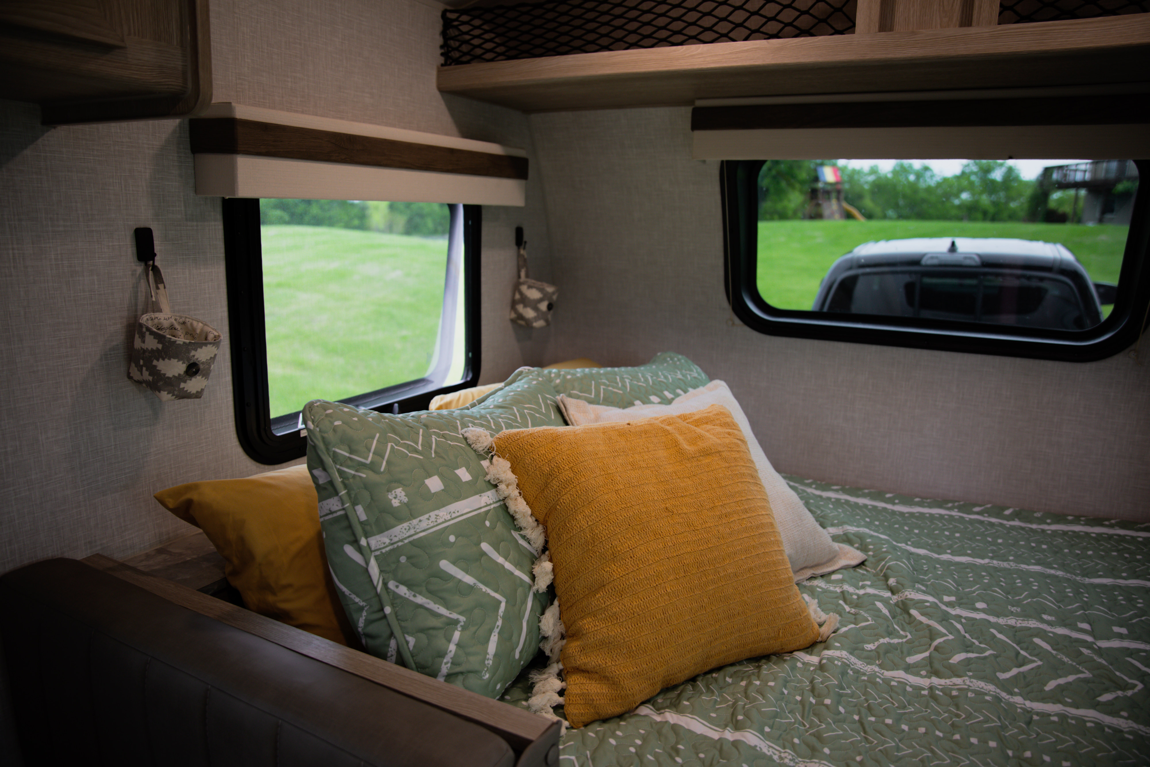 Inside a comfy RV rental: a bed with sage green and yellow pillows, and a window view of a lush green field. Ready for adventure.. Forest River Rockwood Geo Pro 2022