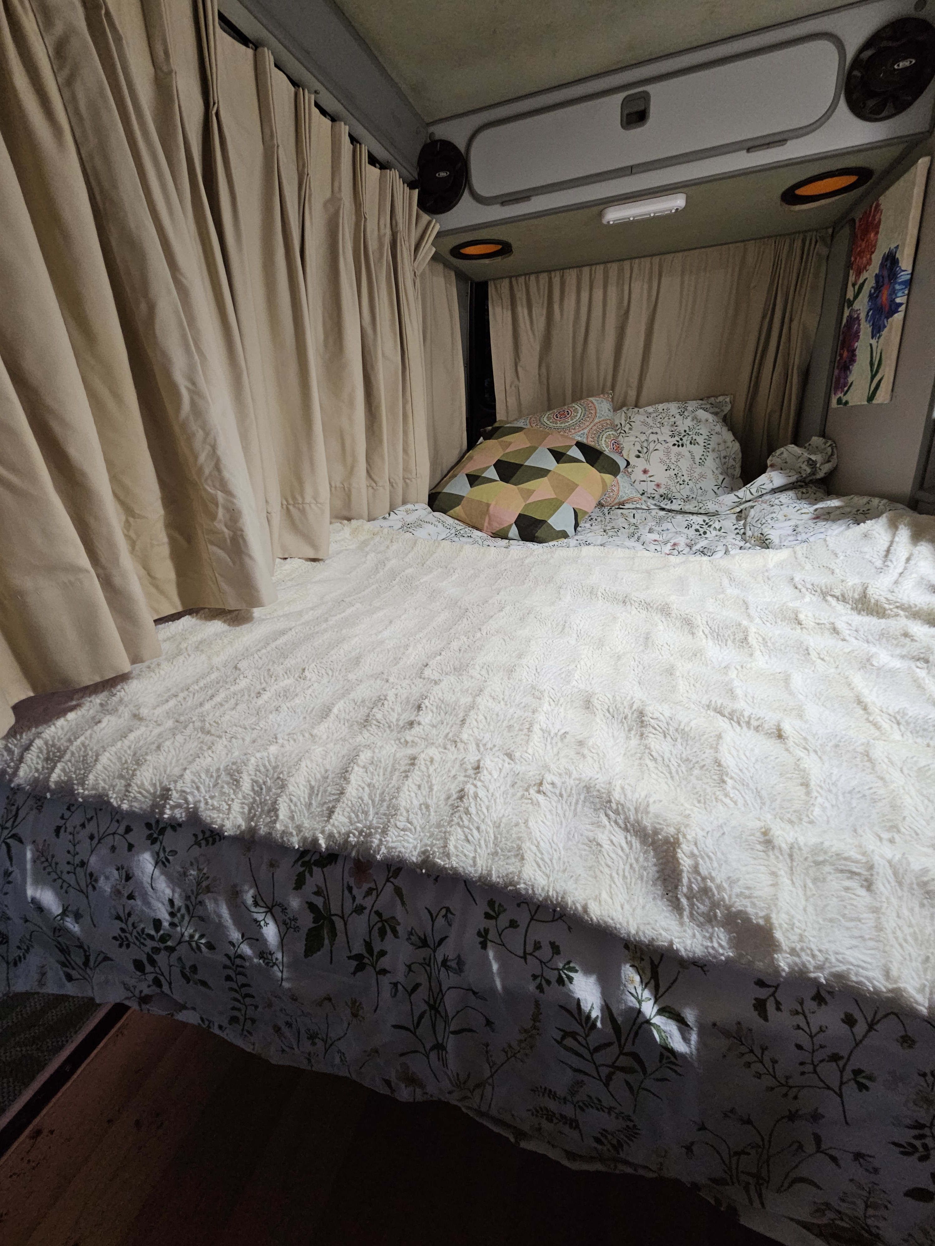 Cozy RV rental bedroom featuring a fluffy white blanket, patterned sheets, and privacy curtains.. Westfalia T3 Westfalia 1987