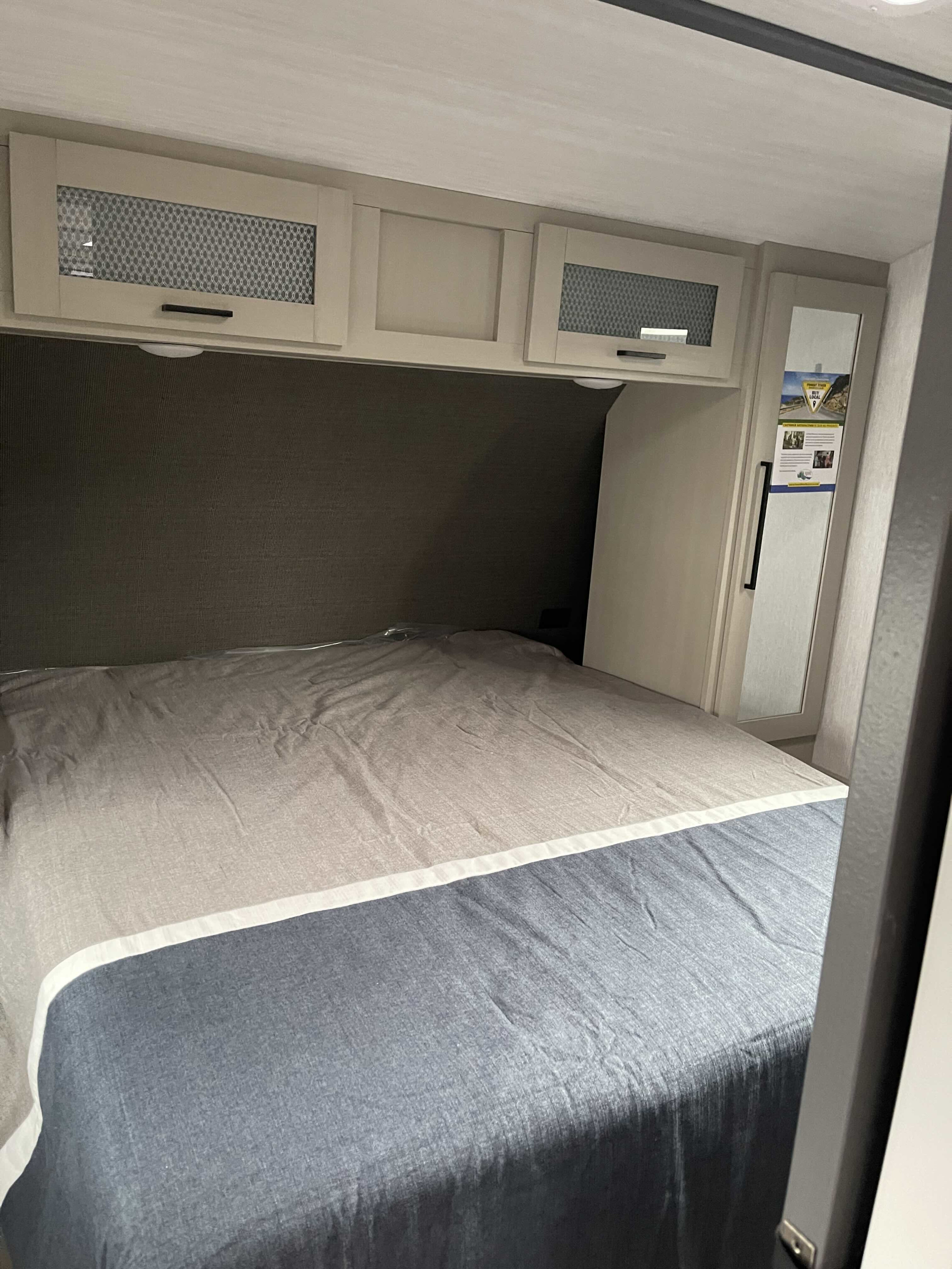 Inside an RV rental: a neatly made bed with dual-tone comforter, padded headboard, and storage cabinets overhead.. Forest River Salem Hemisphere HL 2023