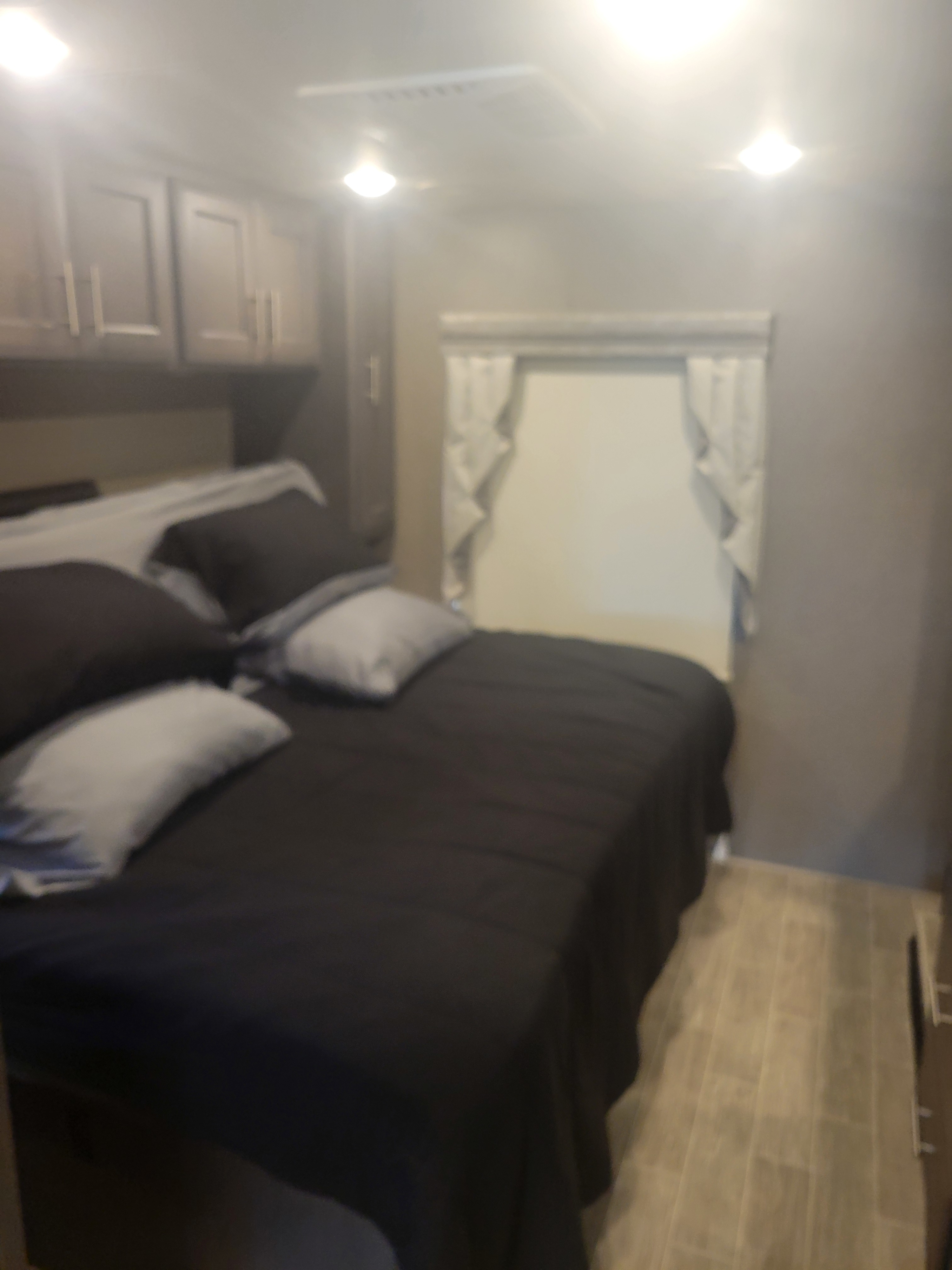 Cozy bedroom in an RV rental, featuring a bed with black comforter, overhead cabinets, and a window.. Thor Miramar 2022