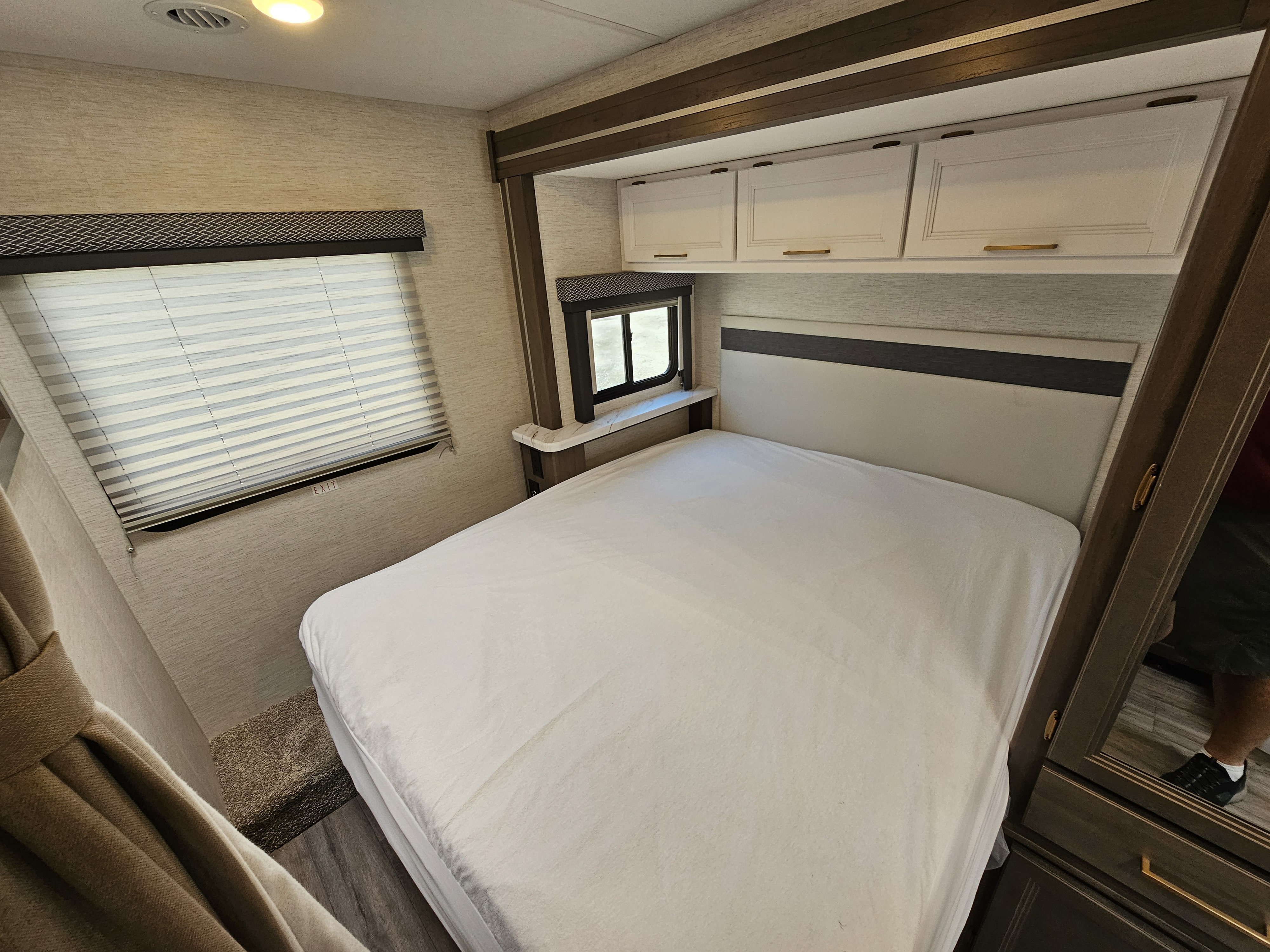 RV rental interior: A modern, cozy bedroom featuring a comfortable bed, bright overhead cabinets, and window.. Thor Motor Coach Four Winds 2025