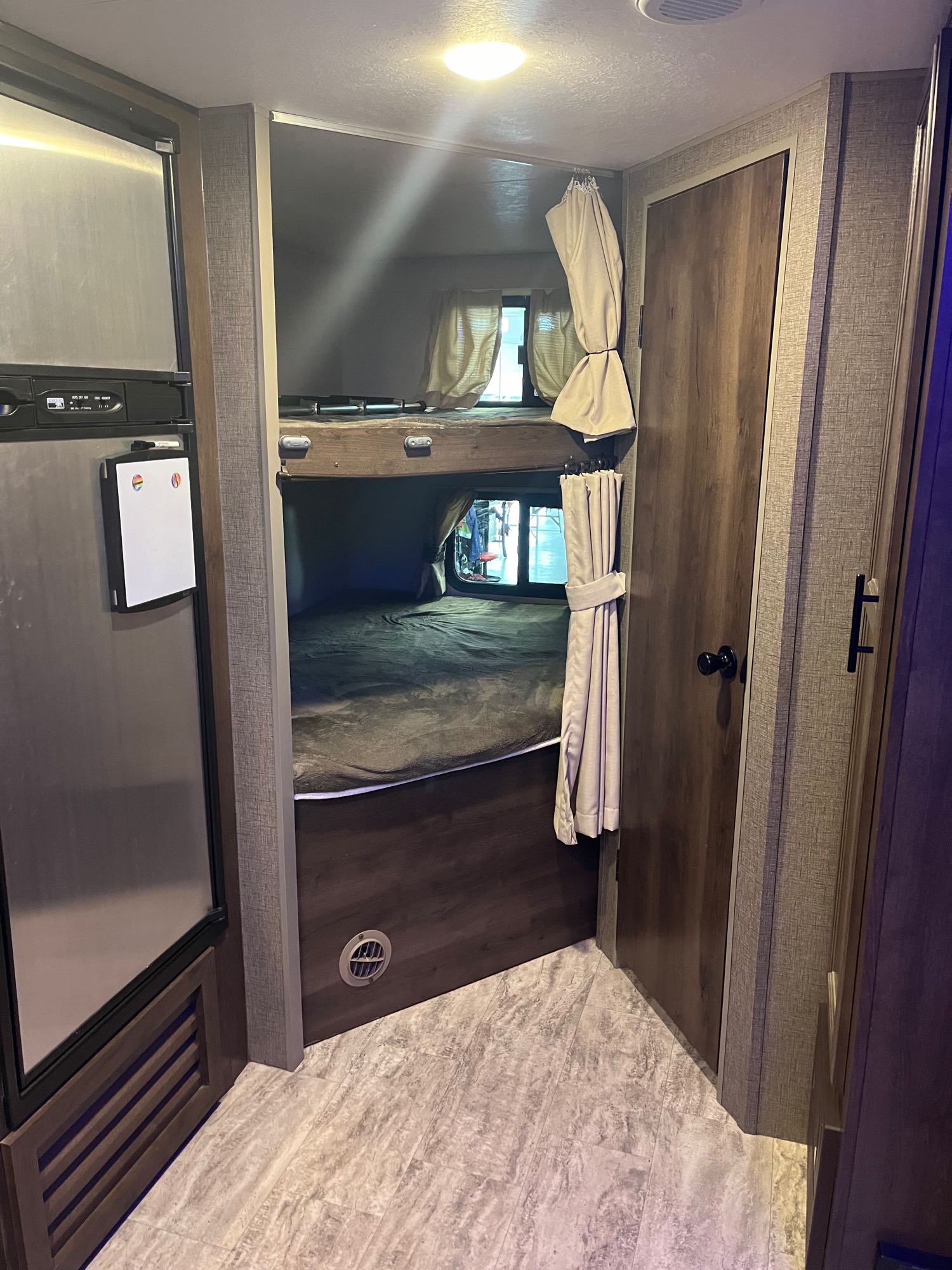 Cozy RV rental interior with bunk beds, a fridge, and a wood-paneled door, showcasing efficient living space.. KZ Connect 214bhk 2018