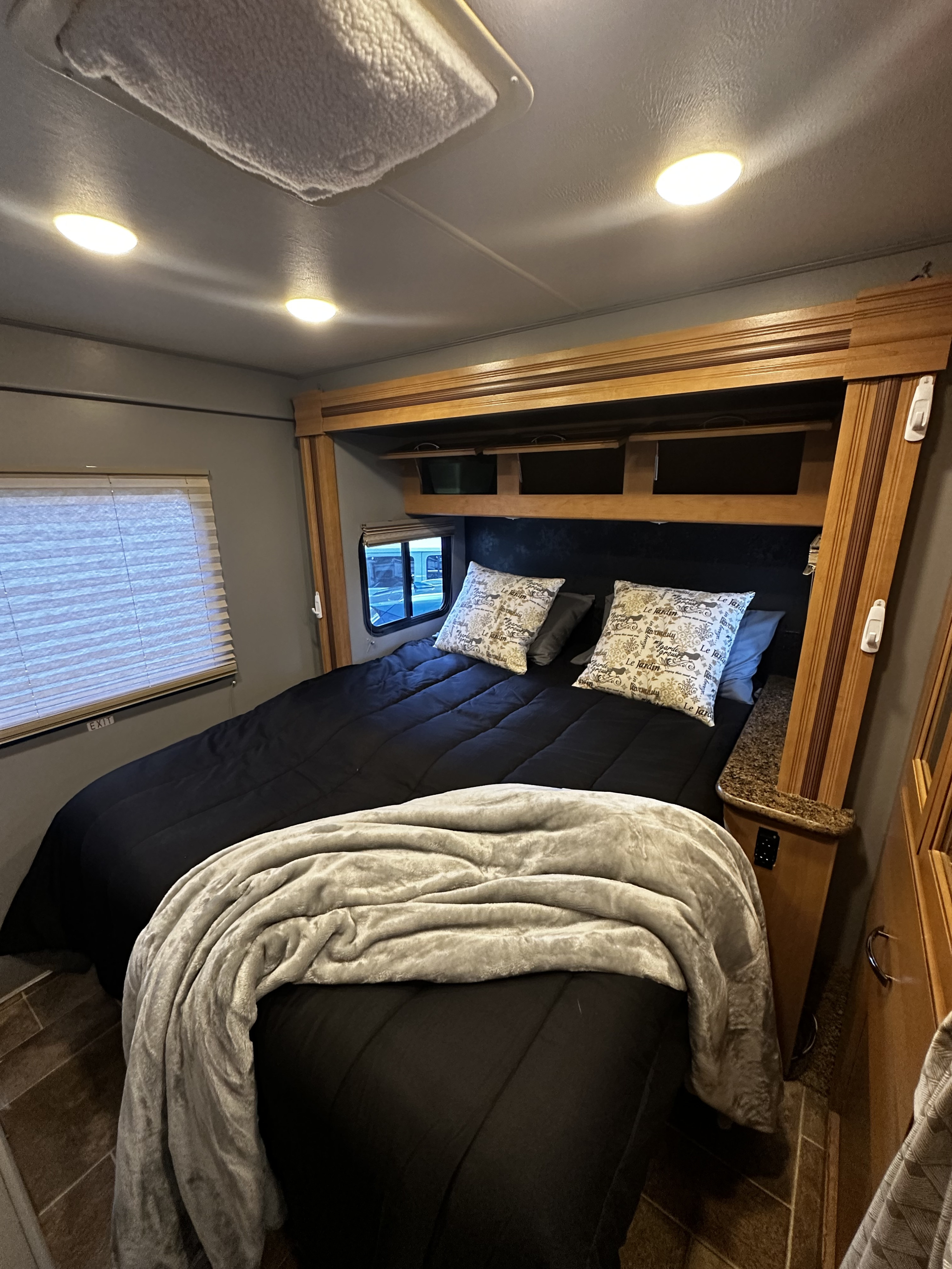 Cozy RV rental bedroom featuring a plush bed, built-in wood storage, and bright overhead lighting.. Thor Freedom Elite 2017