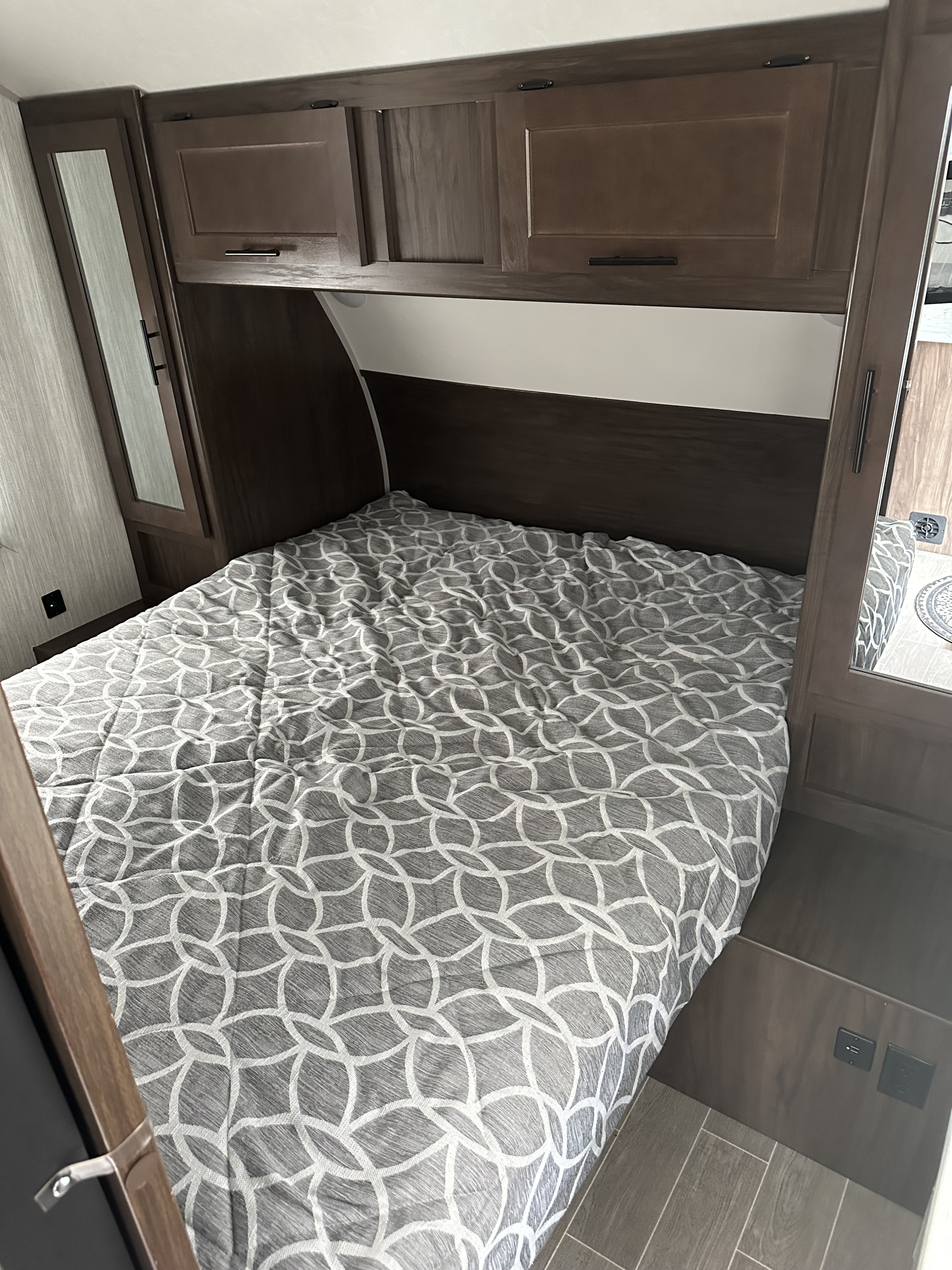 Cozy RV rental bedroom with a patterned bed, dark wood overhead cabinets, and mirrored wardrobes for compact living.. Forest River Cherokee Grey Wolf 2021
