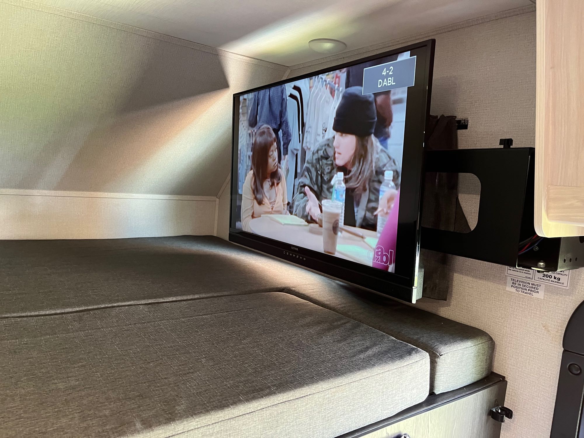 An RV rental bunk bed with a wall-mounted TV showing a program. Ideal for comfortable travel entertainment.. Forest River Sunseeker LE 2023