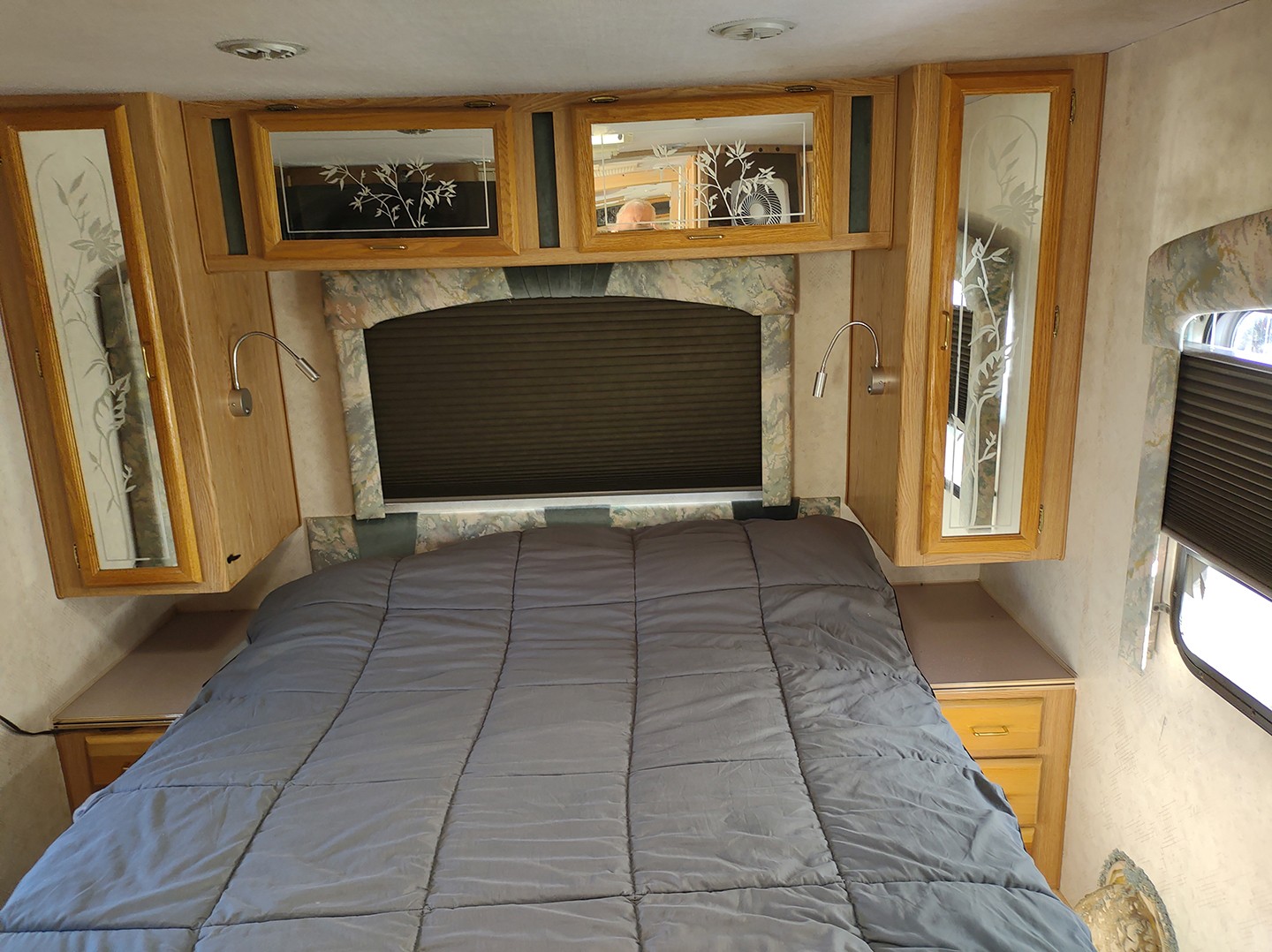 This RV rental bedroom features a comfy queen bed, overhead wood cabinets, and functional reading lights.. National Sea Breeze 1995