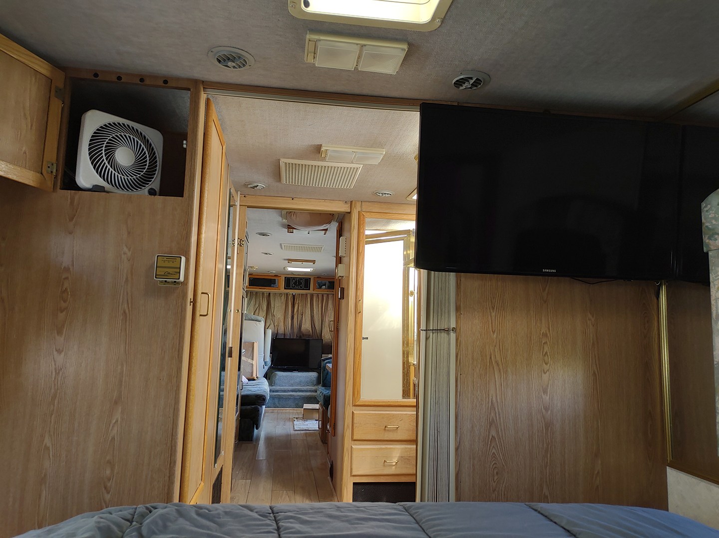 Inside an RV rental: view from bedroom with a TV & fan, looking through wooden cabinetry to the living area.. National Sea Breeze 1995