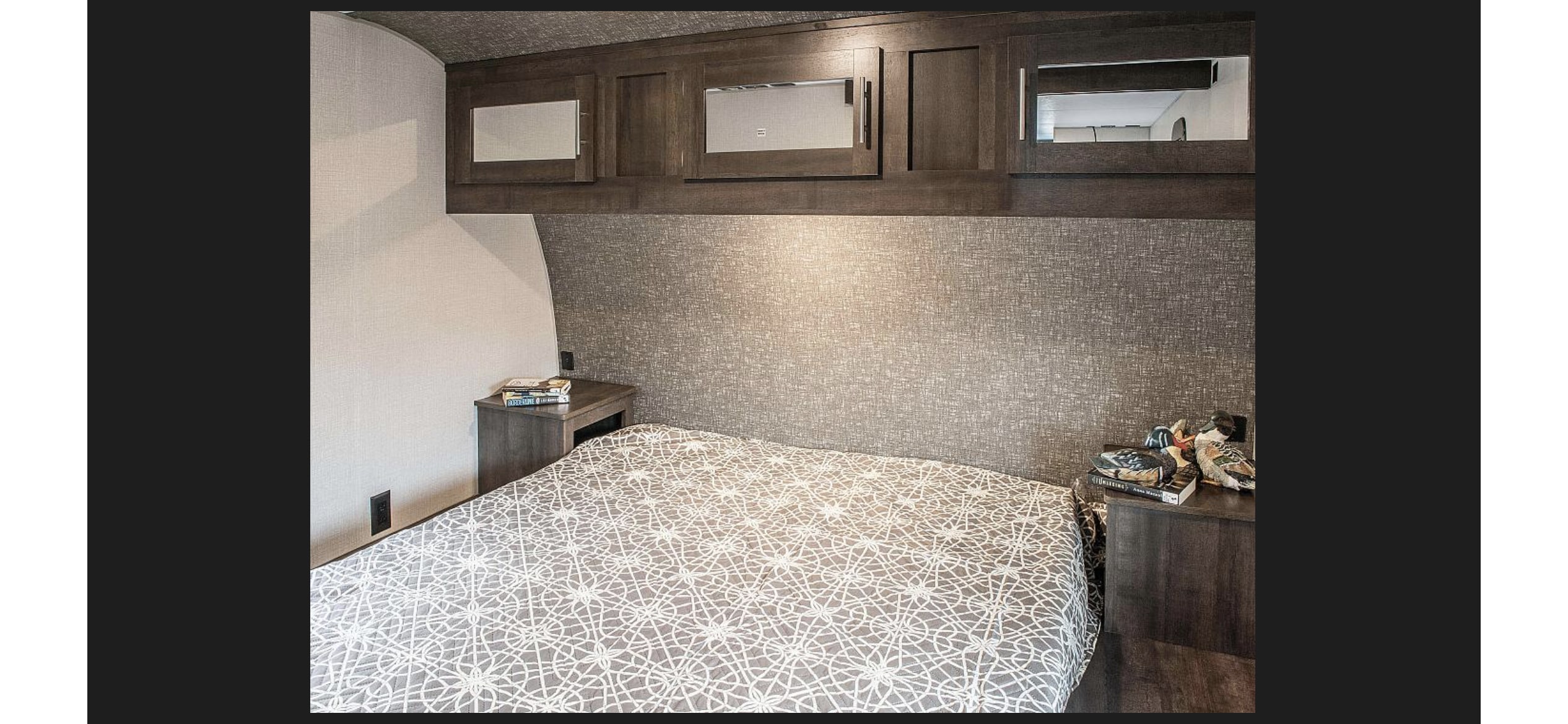Cozy RV rental bedroom with patterned bedspread, nightstands, and overhead storage. Ideal for comfortable travel.. KZ Sportsmen SE 260BHSE 2020