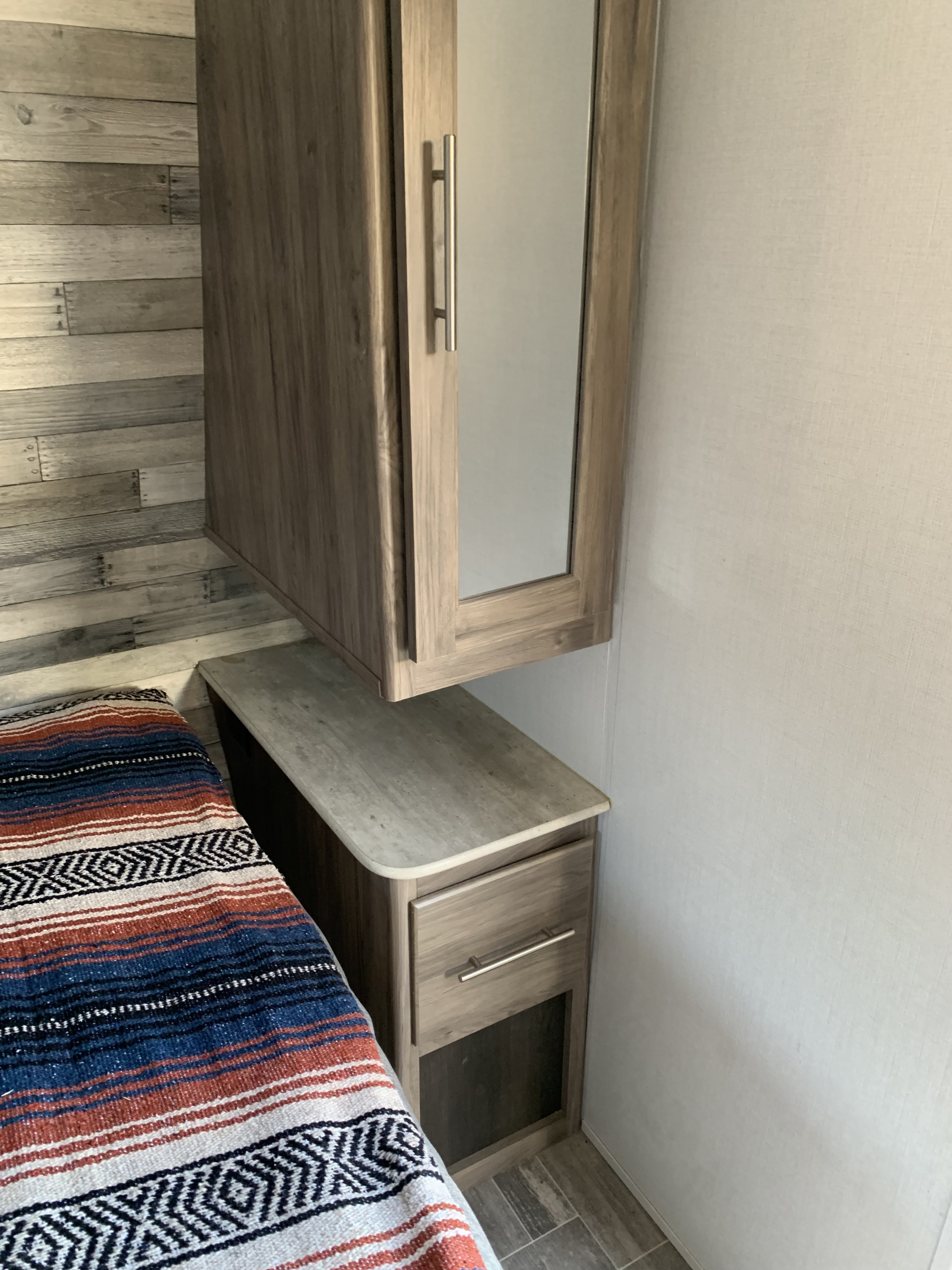 RV rental bedroom with a colorful blanket, wood-paneled wall, and space-saving mirrored cabinet.. Zinger BH 18 2021