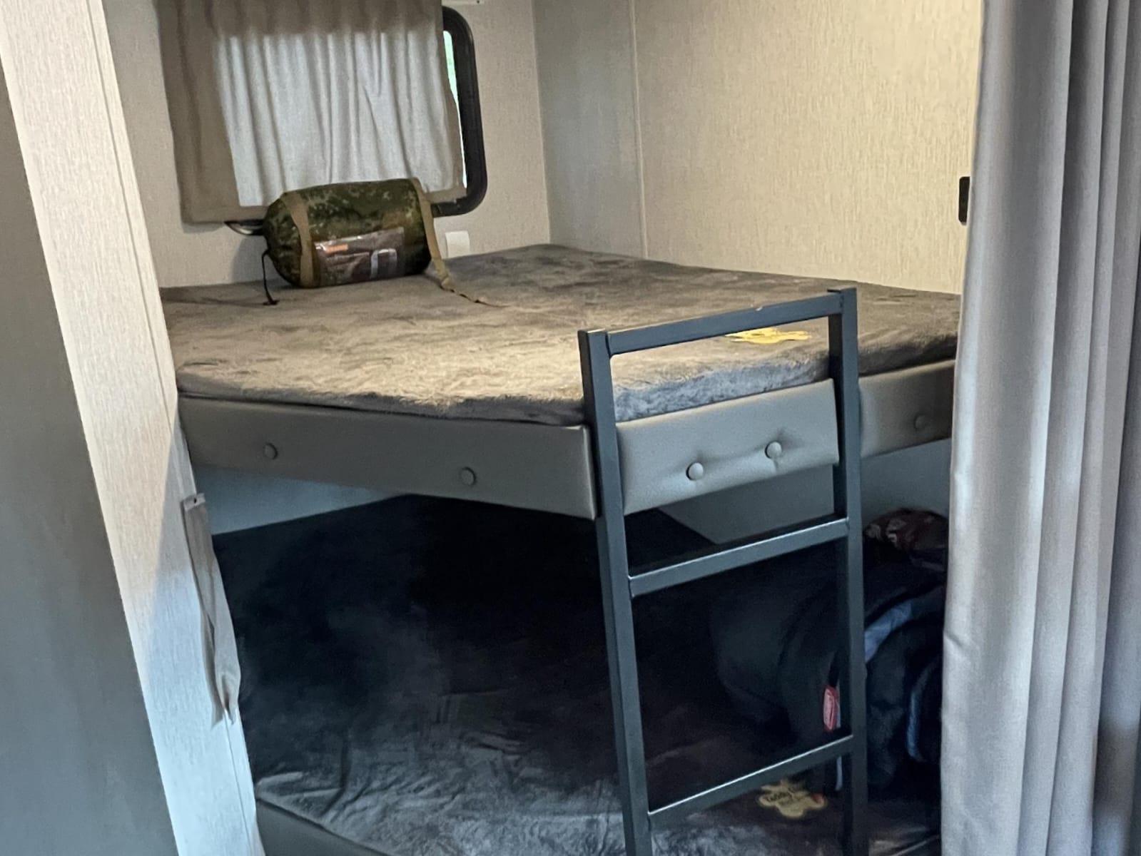 Inside this RV rental, two cozy bunk beds with gray bedding are ready for travelers. A window and ladder are visible.. Forest River Salem Cruise Lite 2023