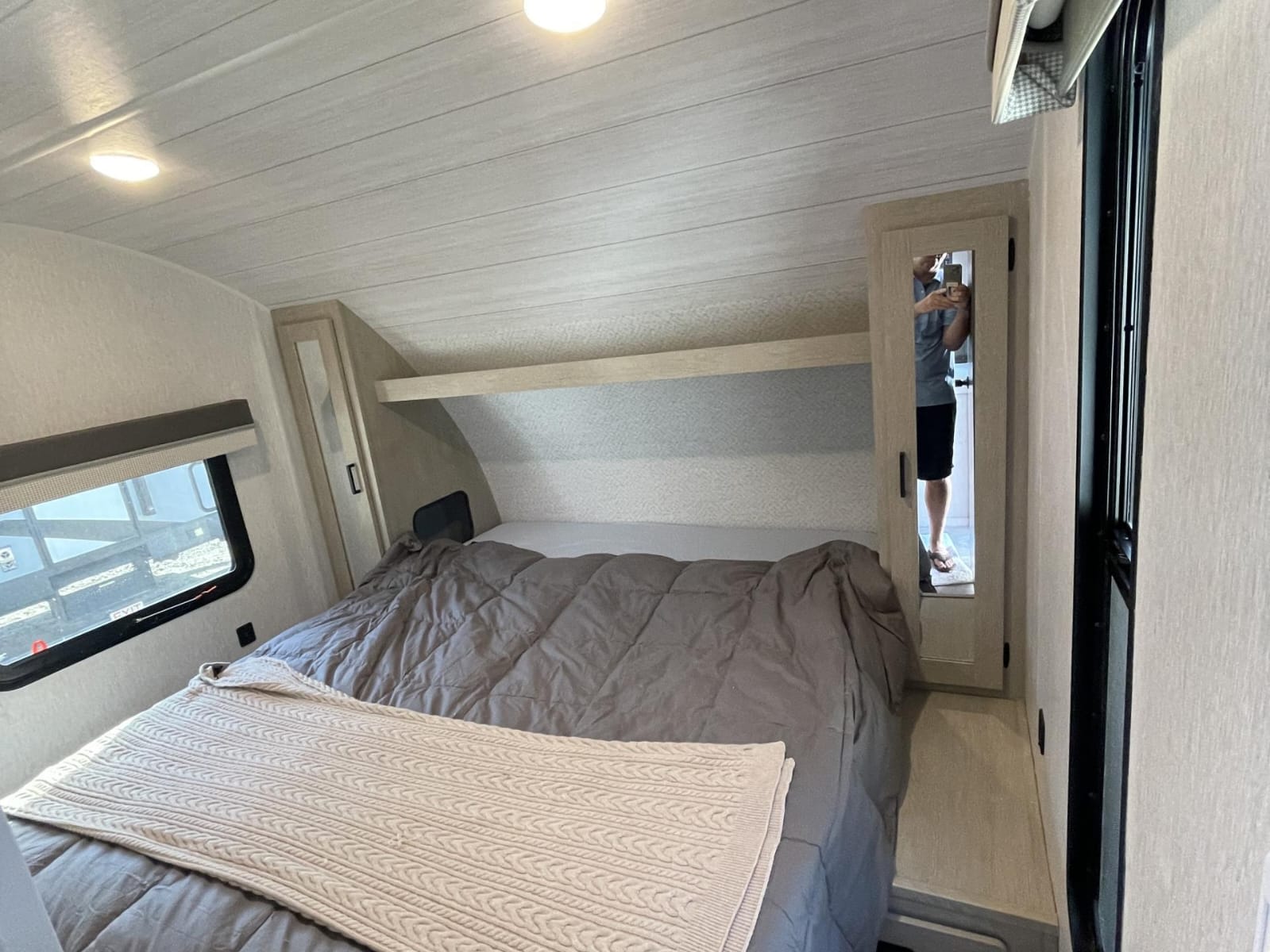 Cozy RV rental bedroom with a large bed featuring grey and beige bedding, overhead storage, cabinets, and a window.. Forest River Salem Cruise Lite 2023