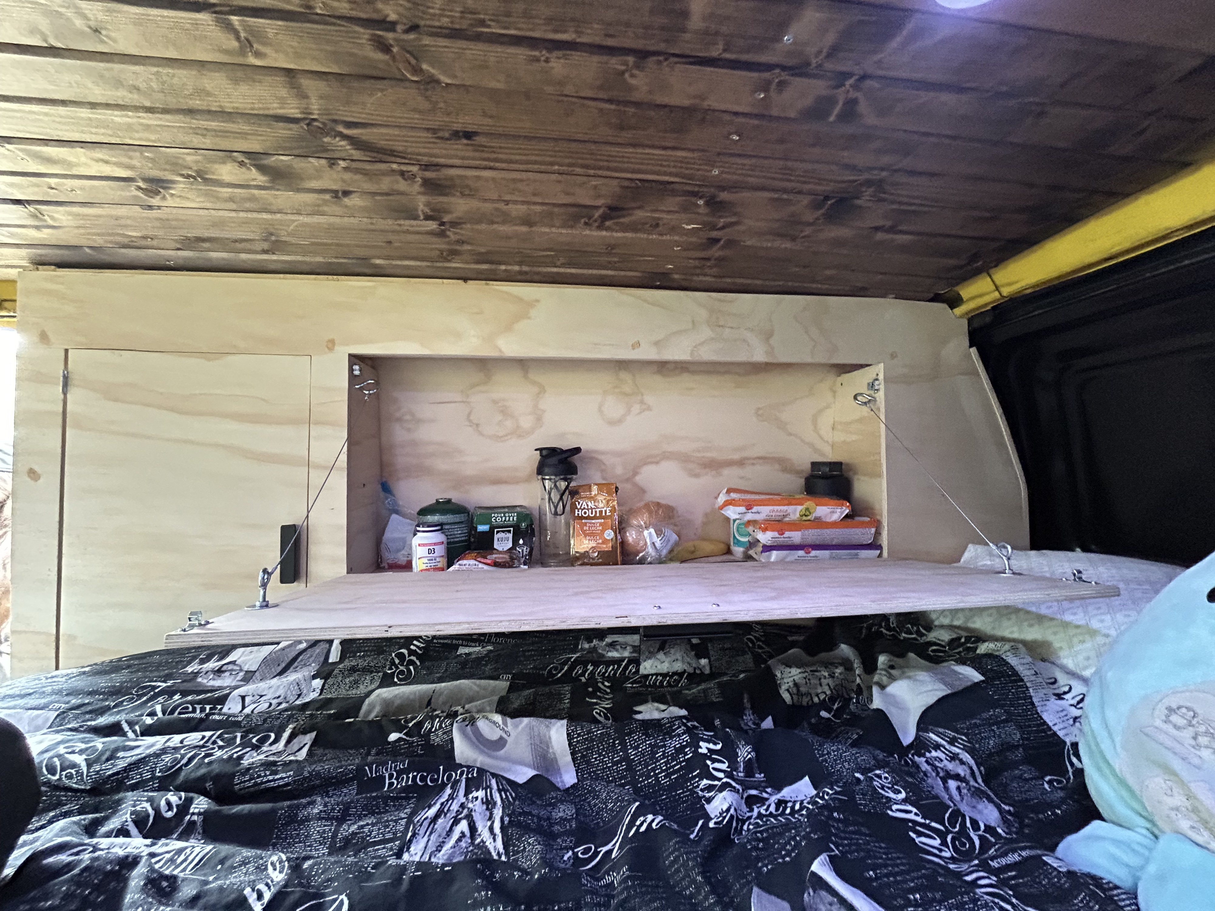 RV rental interior: wooden ceiling, open cabinet with travel supplies, and a fold-down counter over a patterned bed.. Ford Econoline 2007