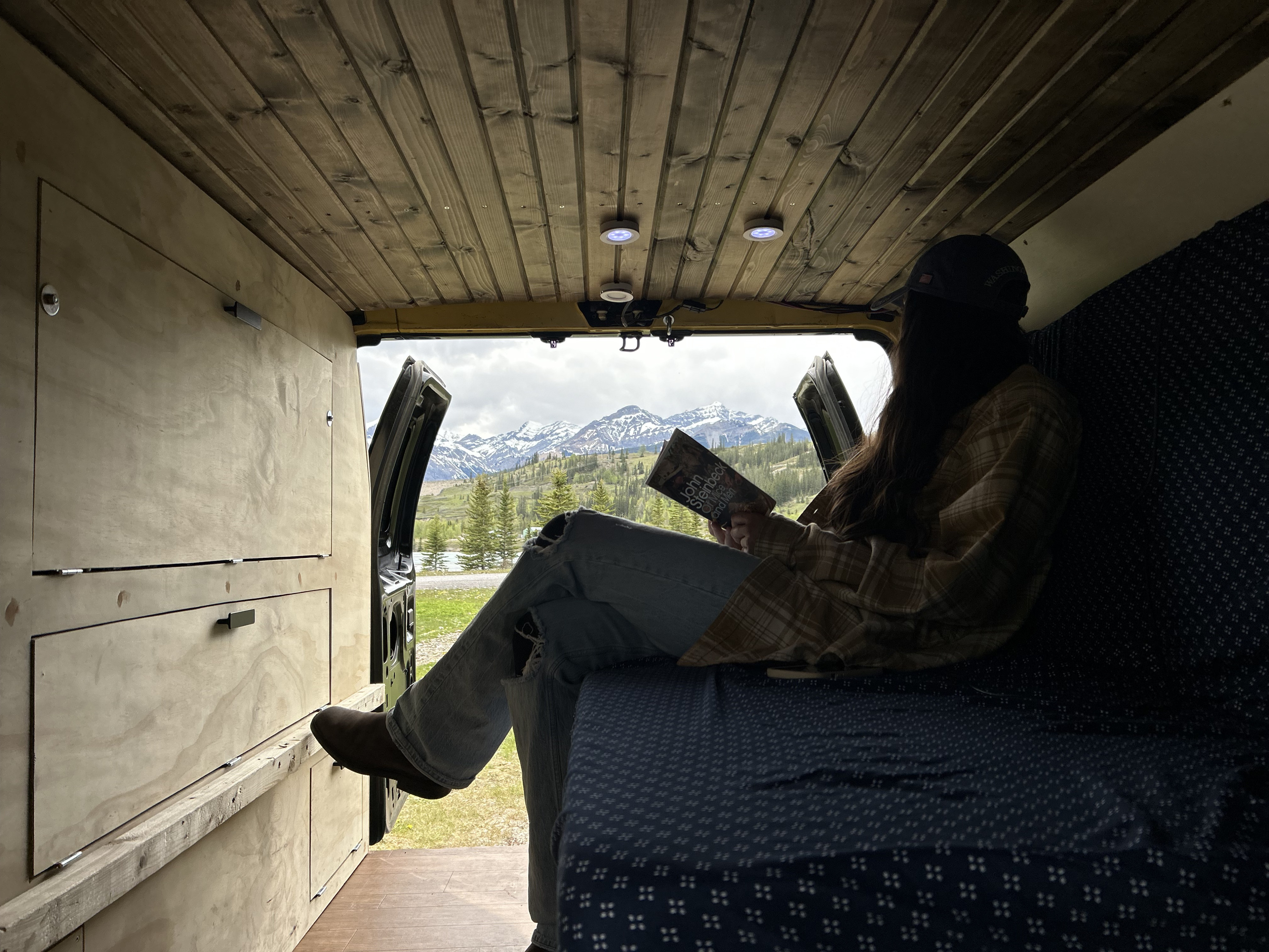 Relaxing in an RV rental with a book and stunning mountain views. A cozy camper van escape amidst nature.. Ford Econoline 2007