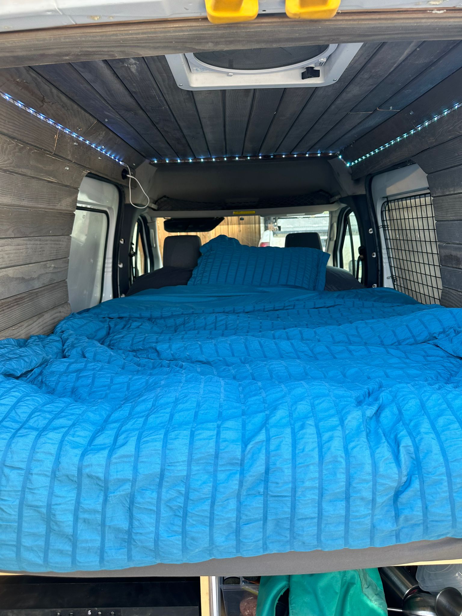 Interior of an RV rental camper van showing a blue bed, wood ceiling with LED lights, and front cabin view.. Ford Transit 2011