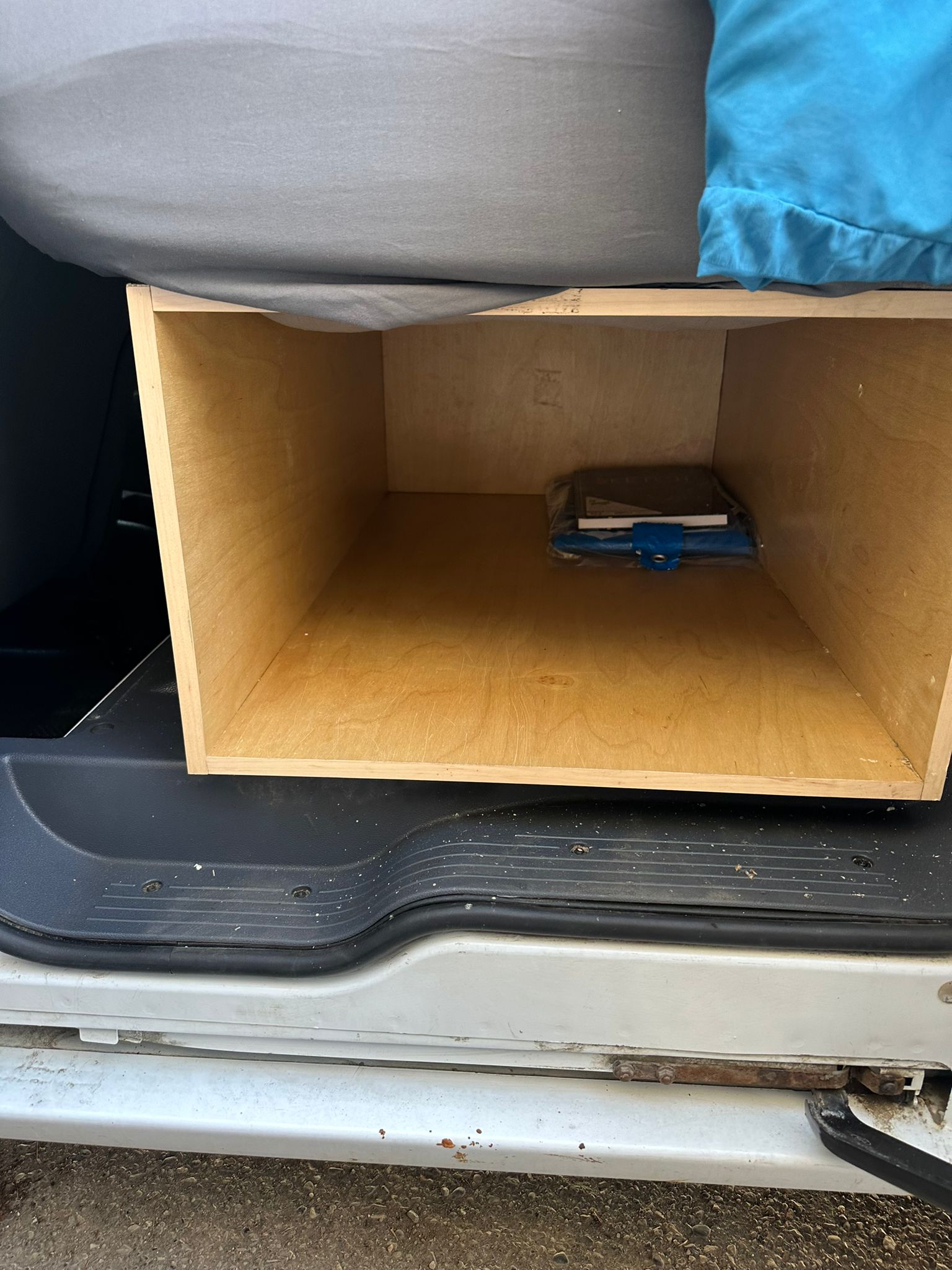 Inside an RV rental: a wooden storage cubby under a gray bed, showing the vehicle's interior floor.. Ford Transit 2011