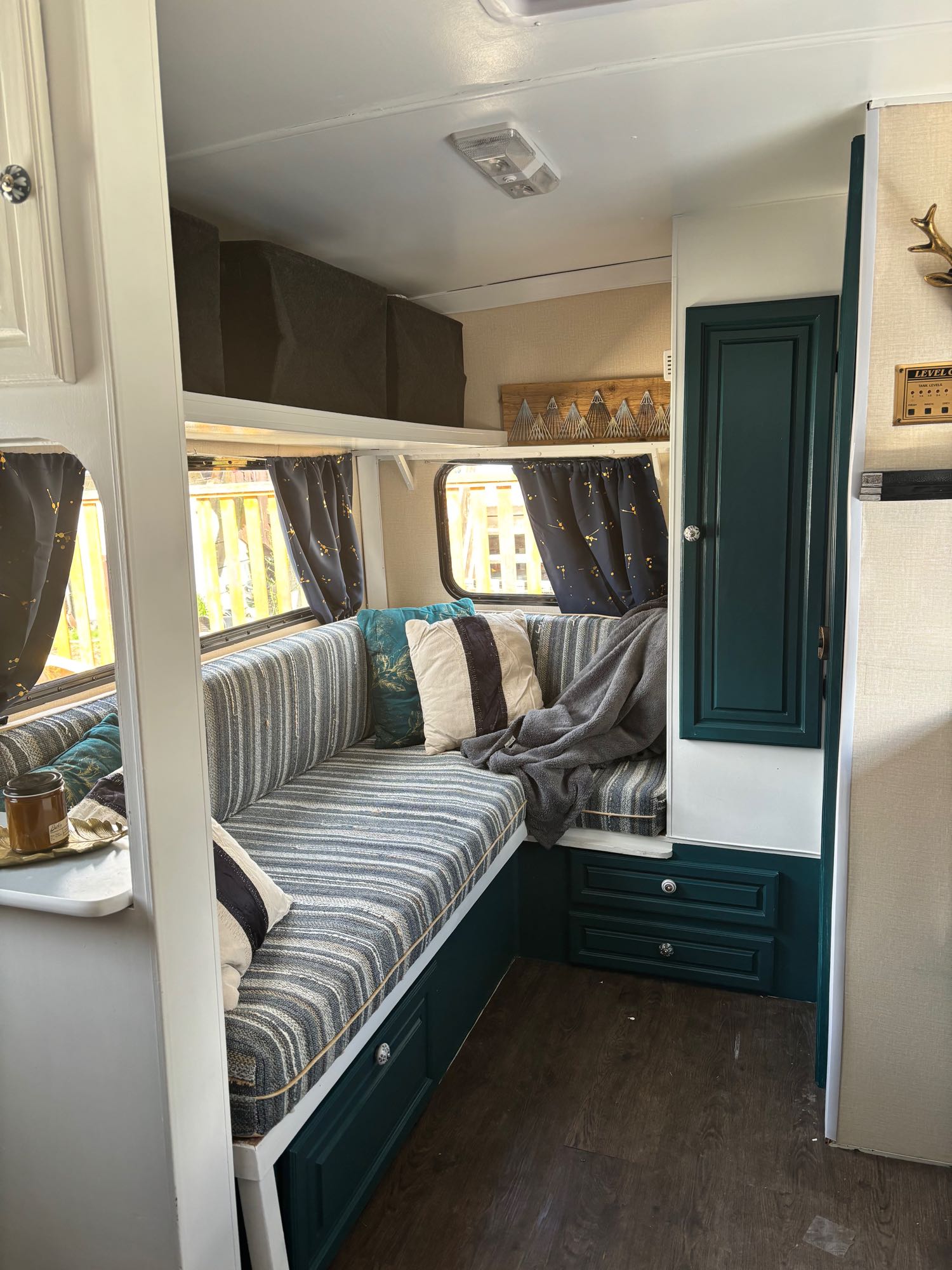 A cozy RV rental interior with striped bench seating, dark teal cabinetry, and wood-look flooring.. Bigfoot DXL 1987