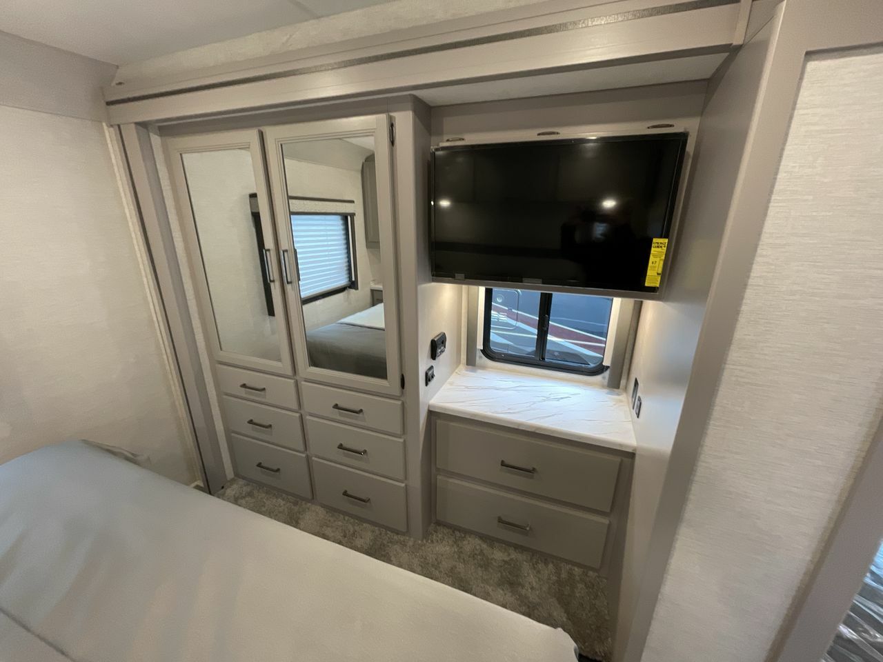 RV rental bedroom featuring mirrored wardrobe, TV, dresser, and window. Compact and functional design.. Thor ACE 2024