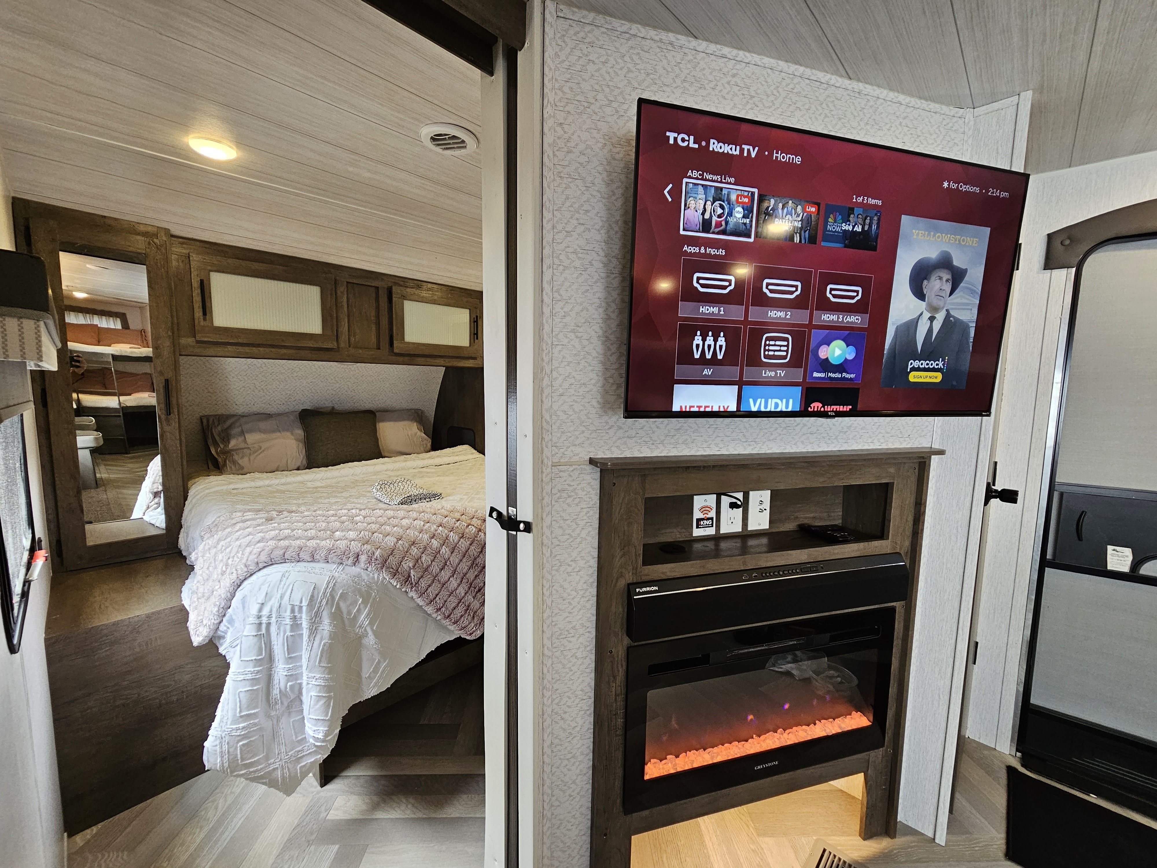 Cozy RV rental interior: living area with TV over electric fireplace, and a bedroom glimpse with bed and reflected bunk beds.. Forest River Salem 2022
