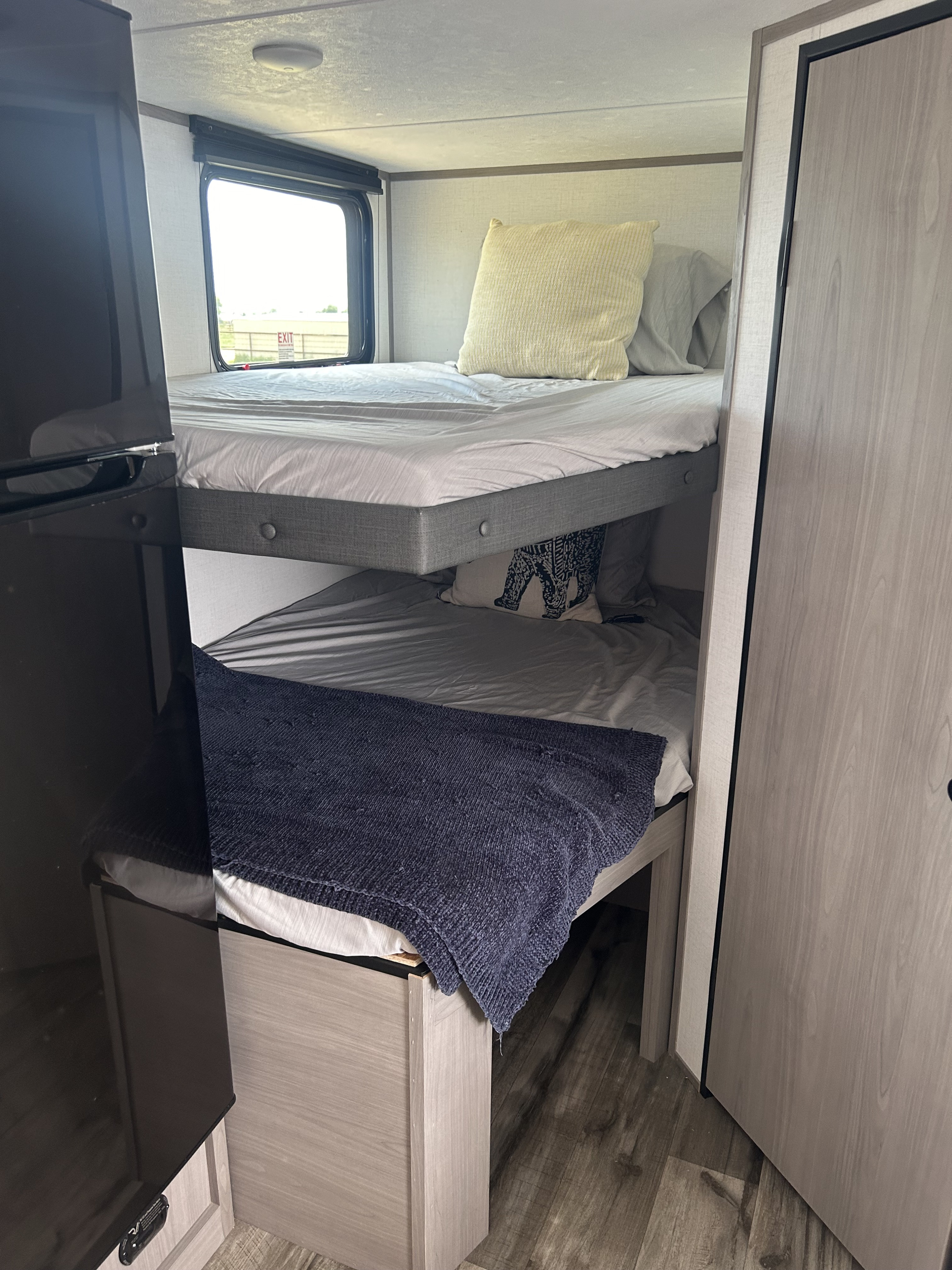 RV rental bunk beds feature cozy stacked sleeping. Top bunk has a yellow pillow; bottom has a dark blue blanket and elephant pillow.. Coleman Coleman Lantern 19BB 2024