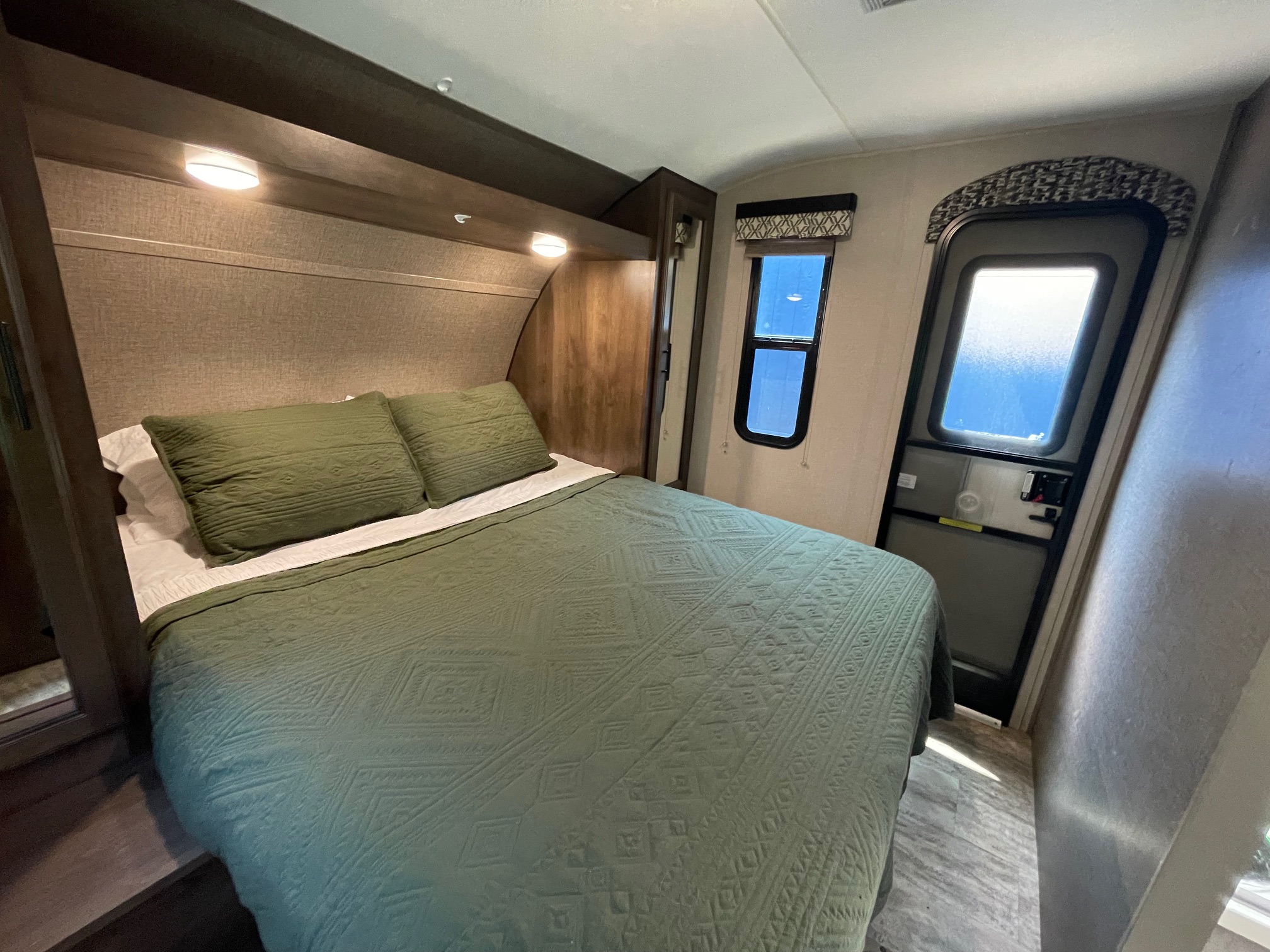 Inviting RV rental bedroom: queen bed with green quilt, reading light, window, and exit door for travel comfort.. Connect 261RL 2018