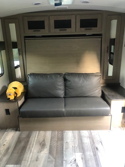 RV rental: Gray sofa, wall bed, cabinets, and wood floor. A yellow stuffed animal sits on the left side table.. Heartland RVs Other 2022