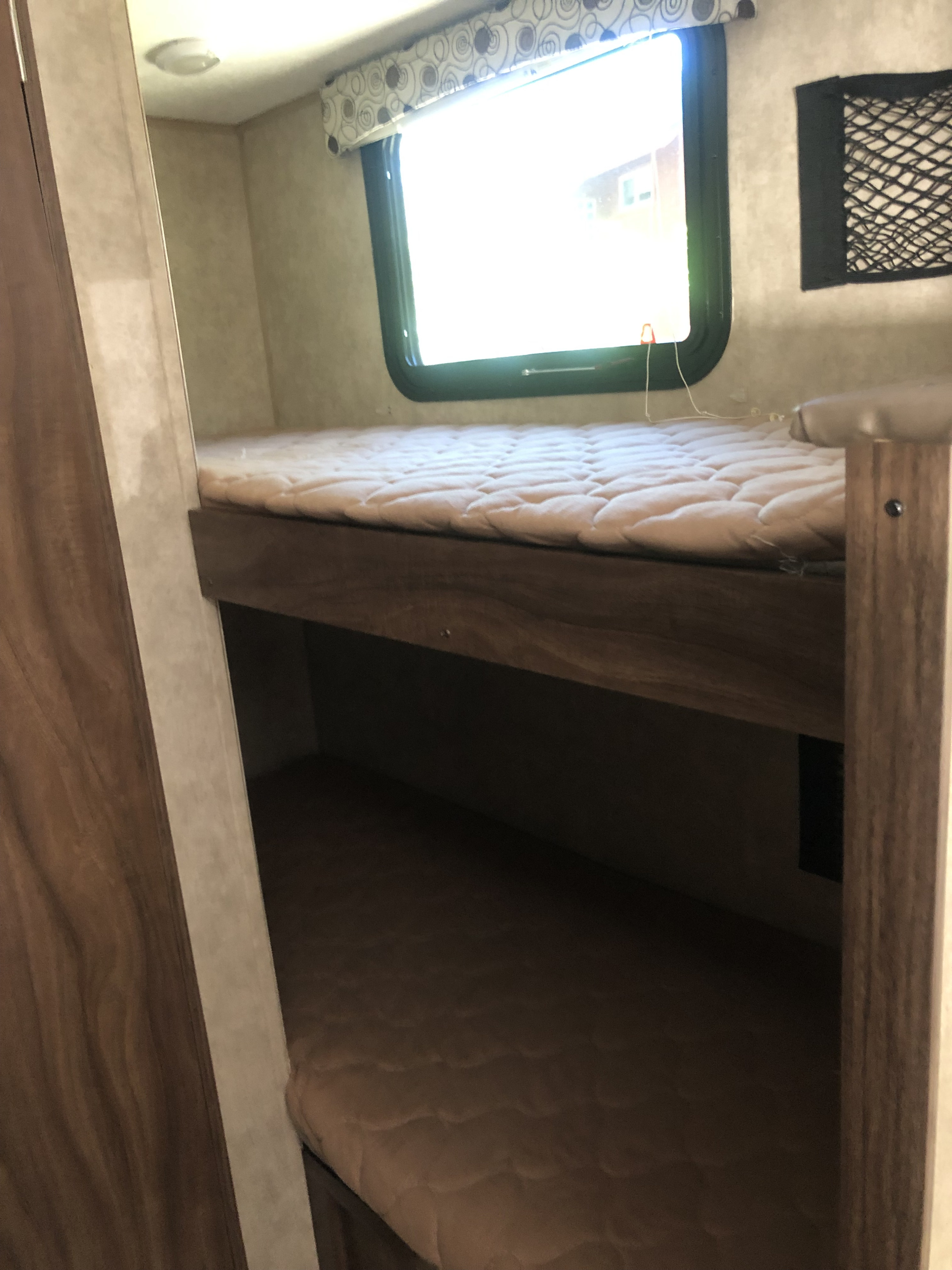 Cozy bunk beds inside an RV rental, featuring comfortable mattresses, a window, and a storage net for small items.. Clipper Cadet 2018
