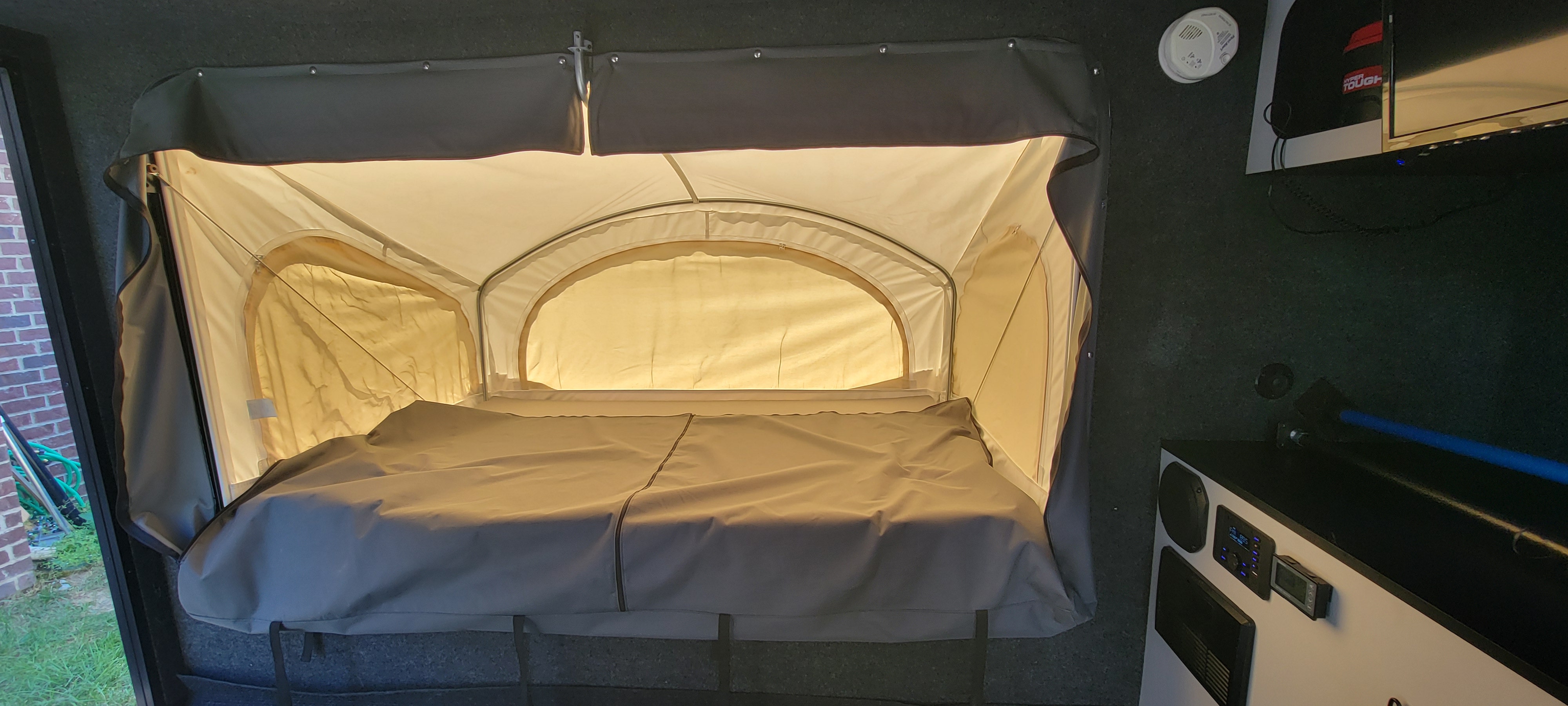 Inside an RV rental: a bright, comfortable pop-up bed with surrounding fabric walls and a control panel for camping.. InTech RV InTech RV Trailer 2020