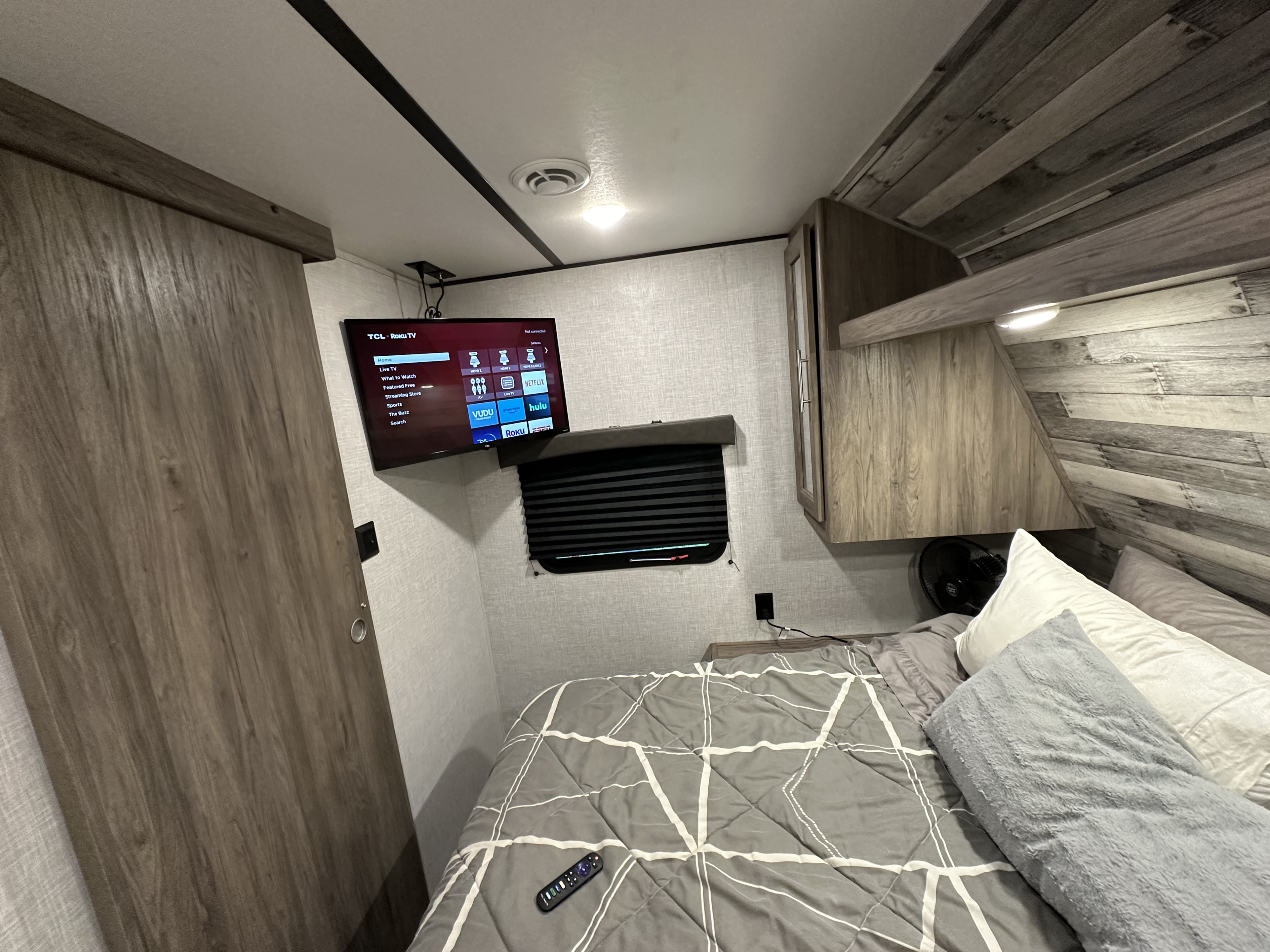 RV rental bedroom with a wall-mounted TV, comfortable bed, compact storage, and wood-like interior.. Crossroads RV Zinger 2021