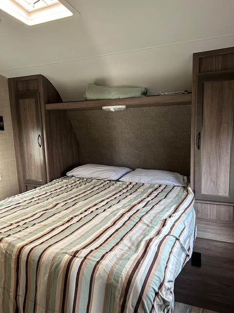 RV rental bedroom: a cozy space with a striped bed, built-in cabinets, overhead shelf, and skylight.. Pacific Coachworks Tango 2017