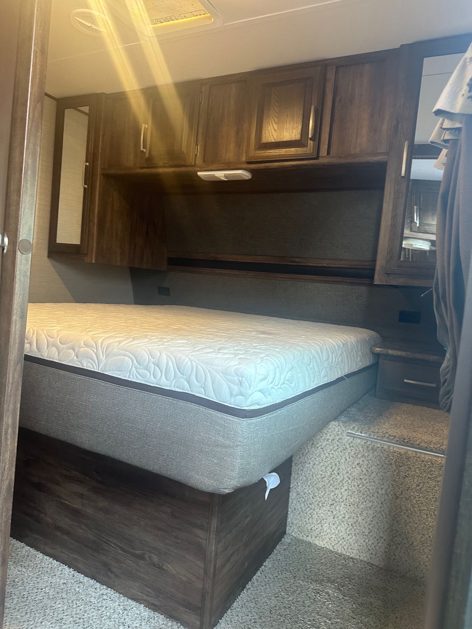 Inside an RV rental bedroom, featuring a white patterned bed, wood overhead cabinets, and compact mirror-sided storage.. Keystone RV Cougar 2016