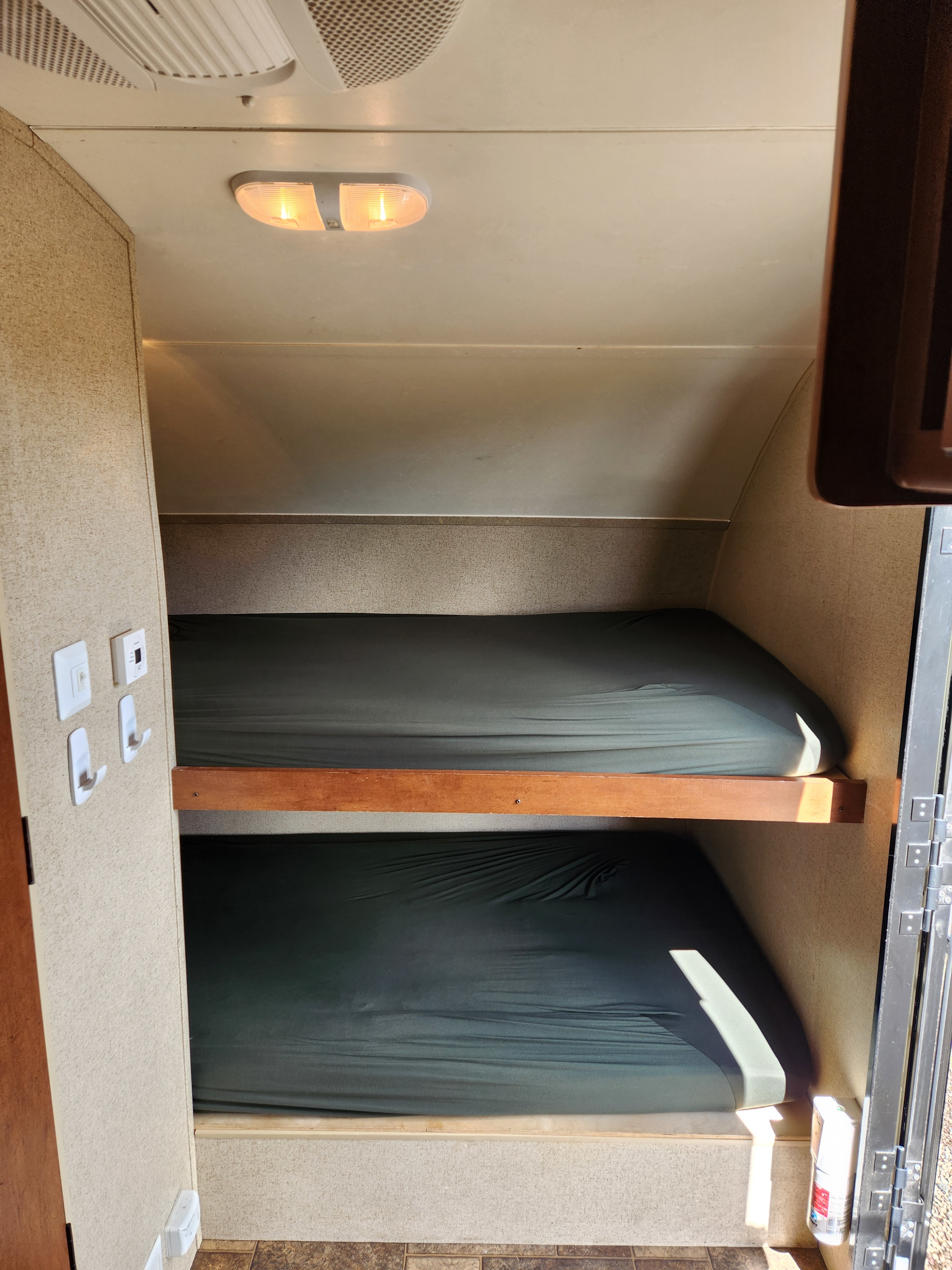 Inside an RV rental: two dark-covered bunk beds, overhead lighting, and wall controls. A practical, compact sleeping area.. Forest River R POD 172 2013