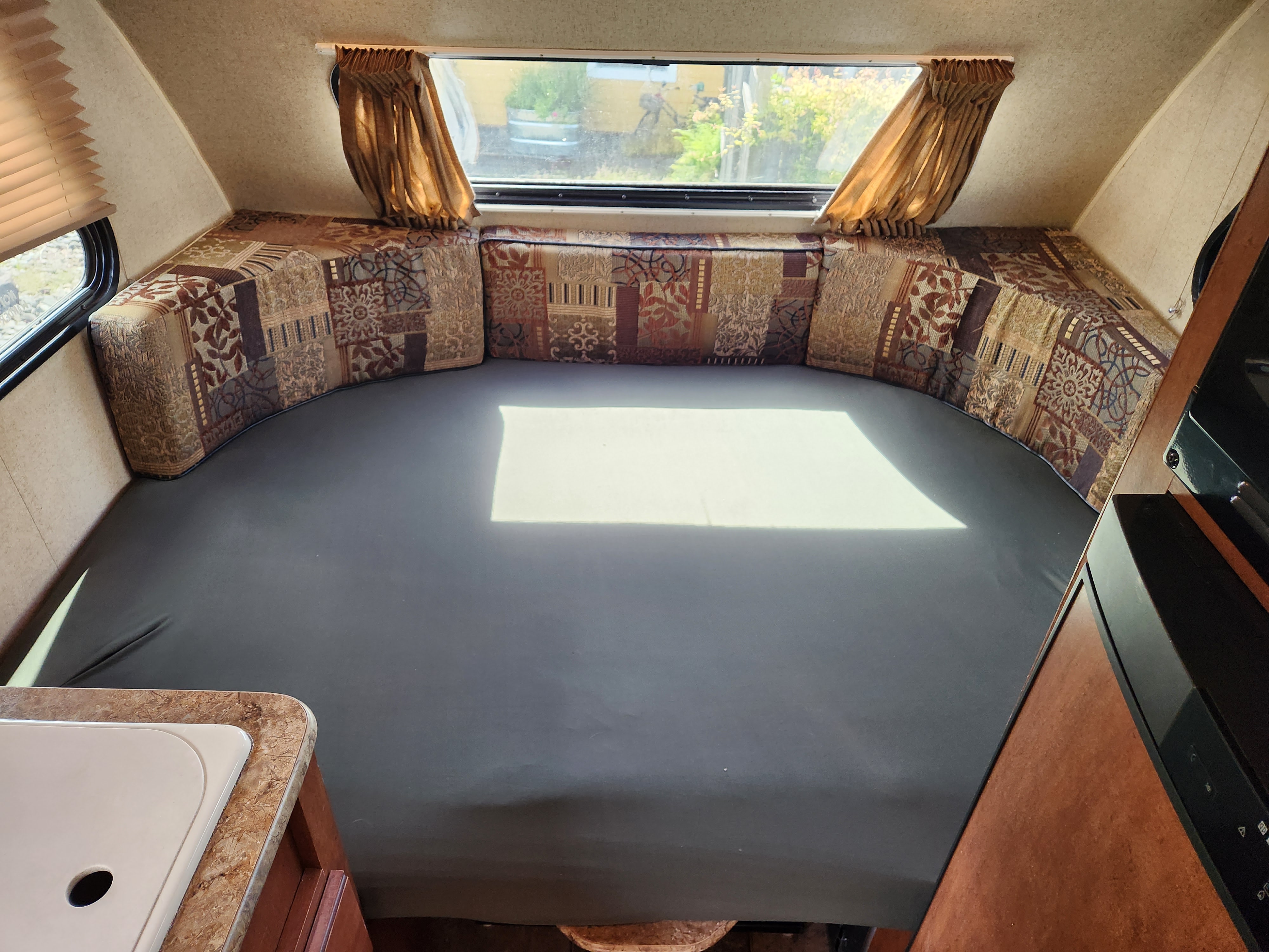 Inside an RV rental: a U-shaped bed with patterned cushions, ample natural light, and a compact kitchen counter.. Forest River R POD 172 2013