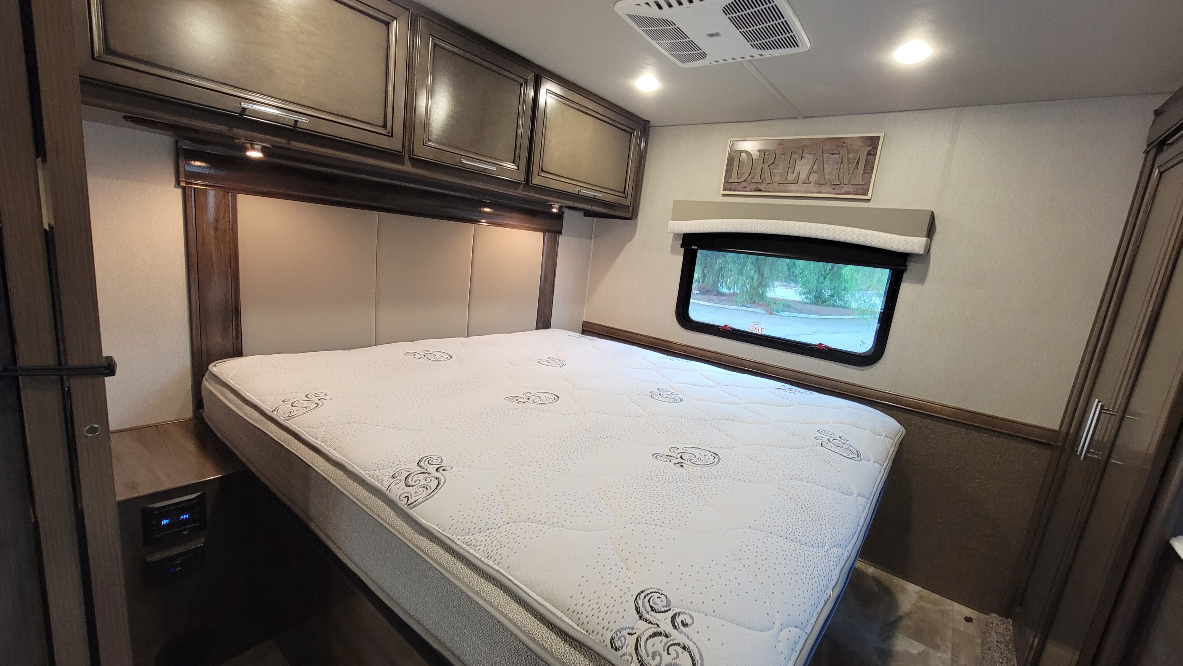 Comfortable RV bedroom for your rv rental, with bed, padded headboard, overhead cabinets, window, 'DREAM' sign, and AC.. Fleetwood Flair 2023