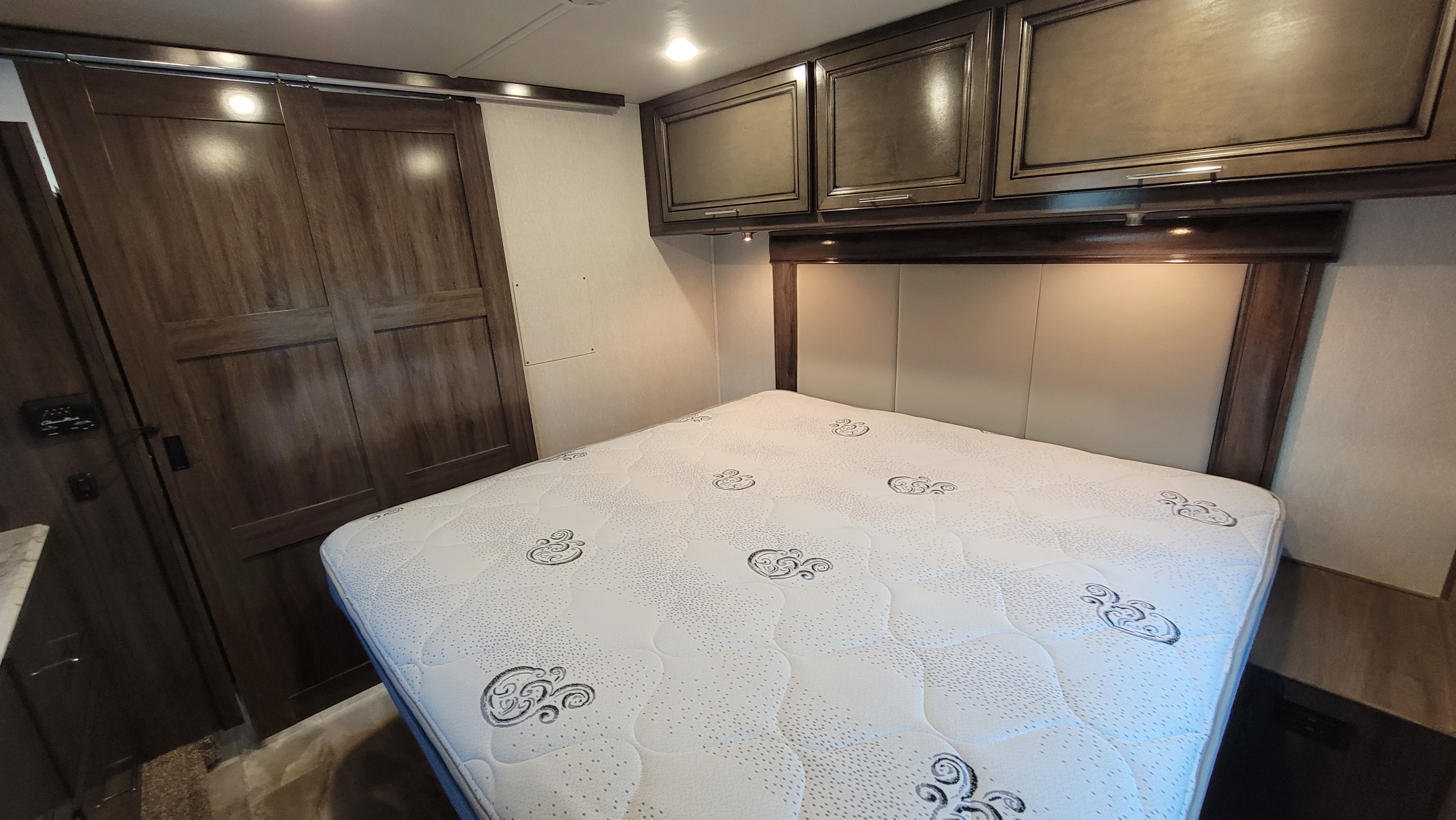 Spacious RV rental bedroom with comfortable mattress, overhead cabinets, and sliding doors. Perfect for travel.. Fleetwood Flair 2023