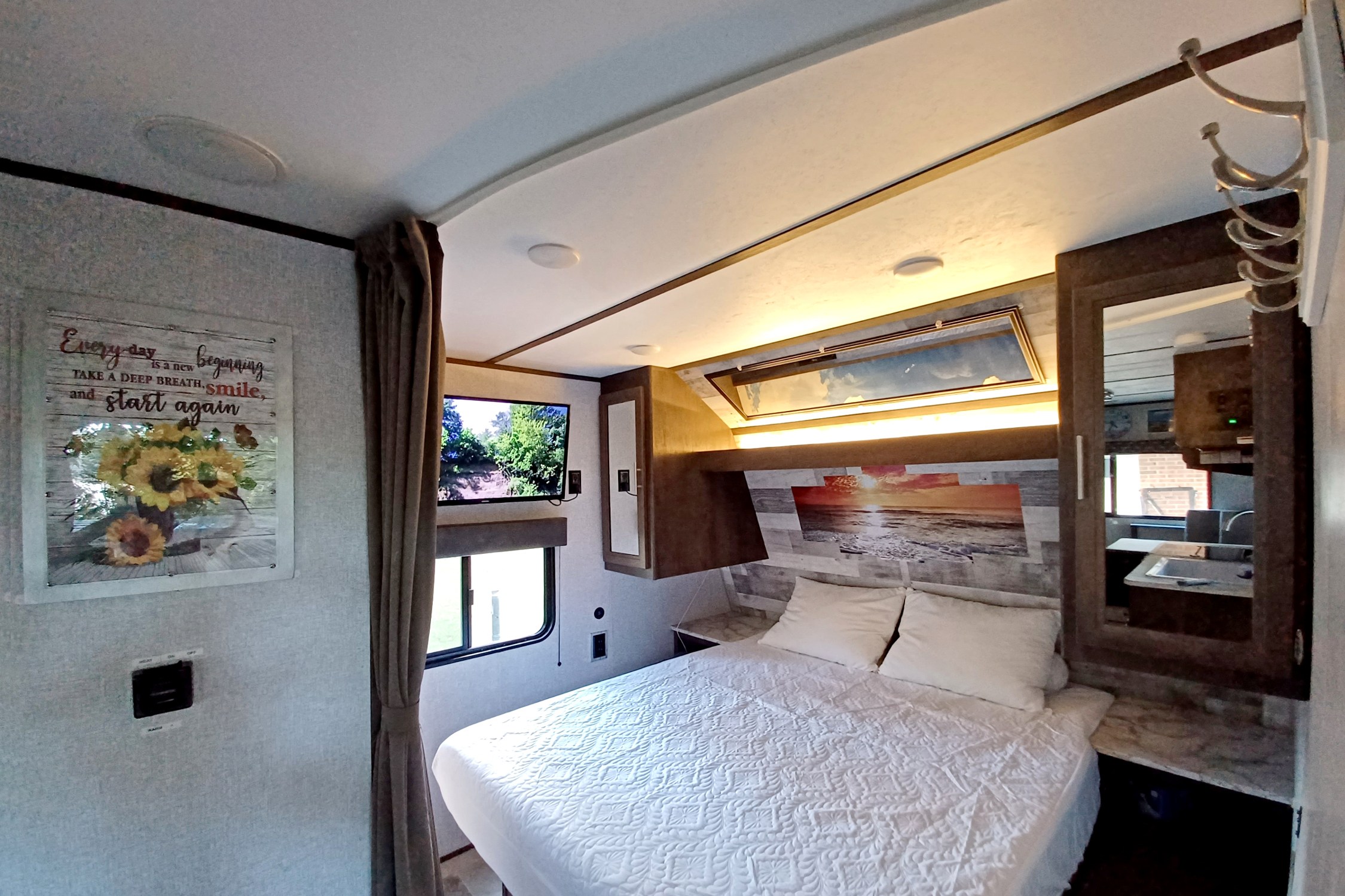 Spacious RV rental bedroom with a large white bed, TV, and vibrant sunset headboard for travel comfort.. Dutchmen Coleman Lantern LT 2020