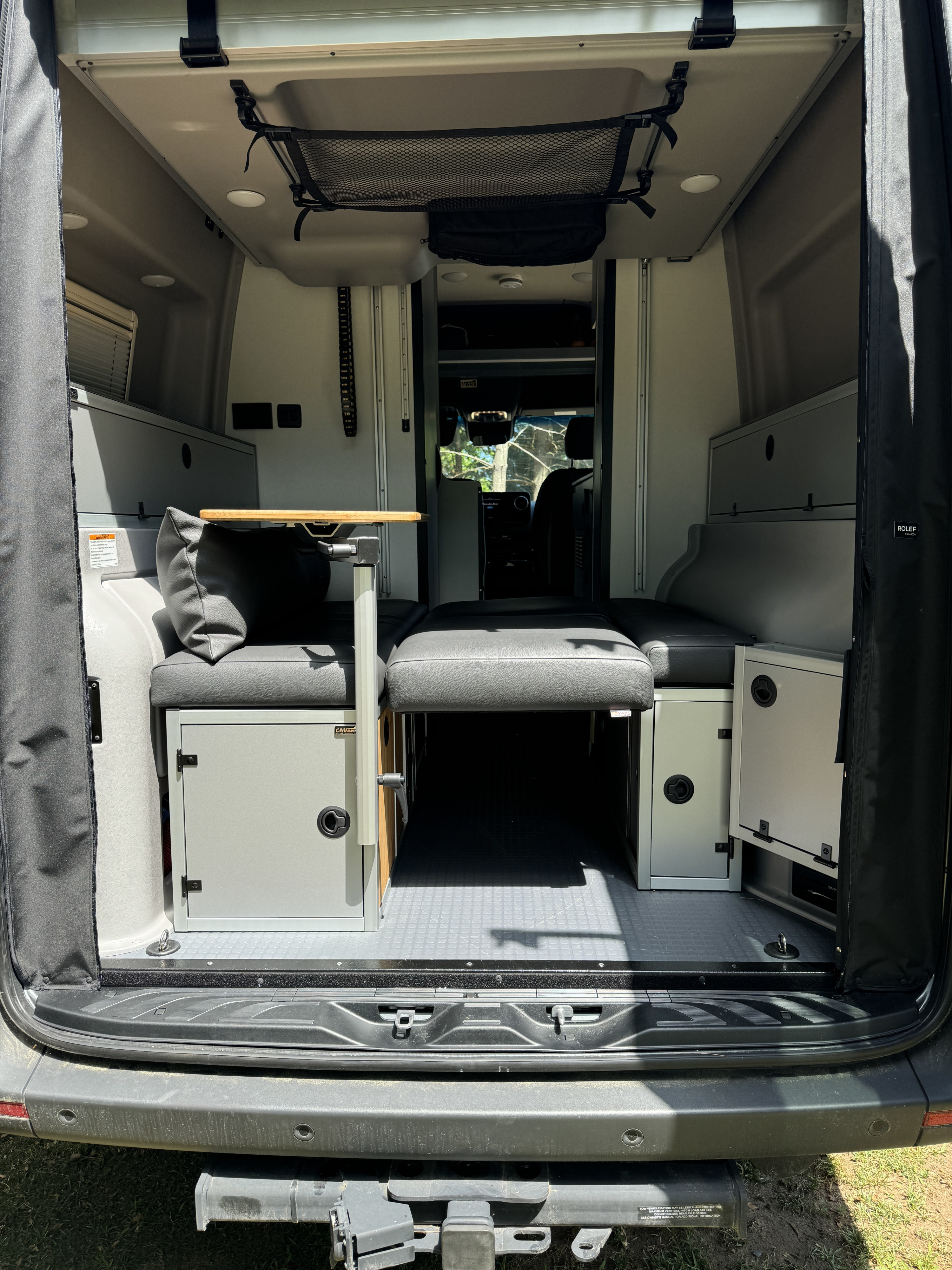 Inside this RV rental: a flexible interior with modular seating, a convertible bed, storage cabinets, table, and overhead net.. Winnebago Revel 2023