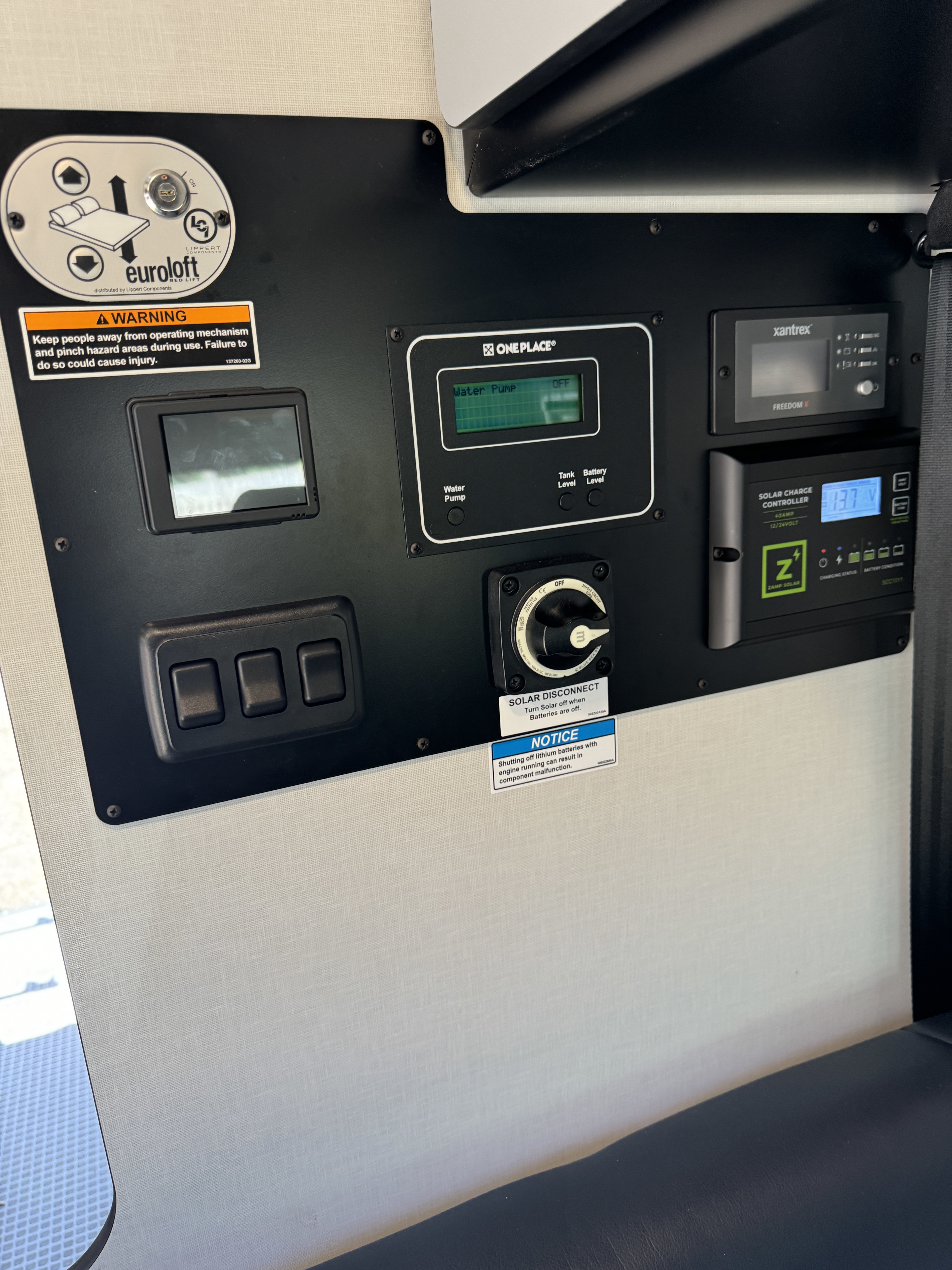 This RV rental control panel shows monitors for bed lift, water, power, and solar charge, with system management switches.. Winnebago Revel 2023