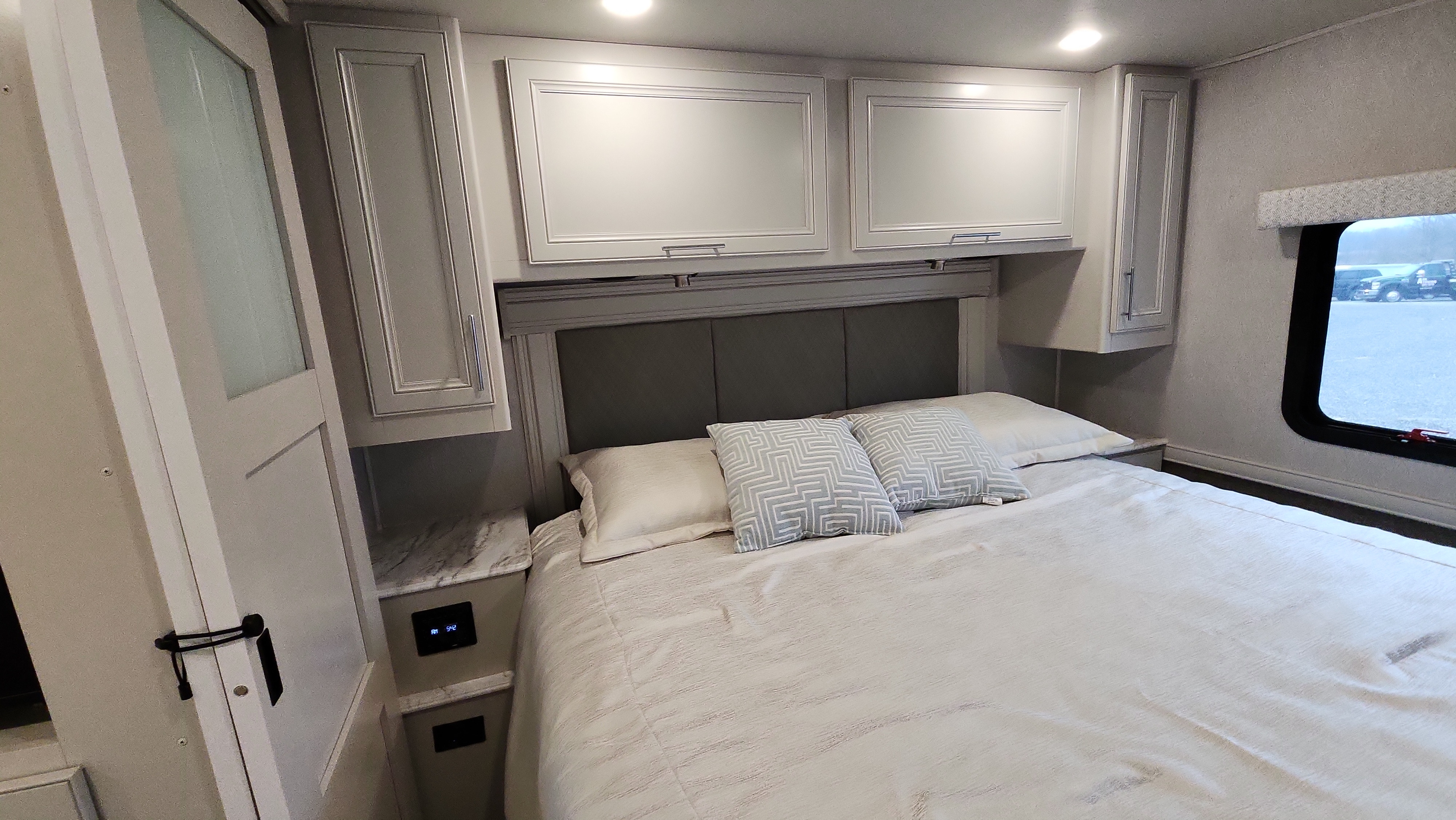 Inside a modern RV rental: cozy bedroom featuring a queen bed, ample overhead cabinets, and soft lighting for your journey.. Holiday Rambler Eclipse 2024