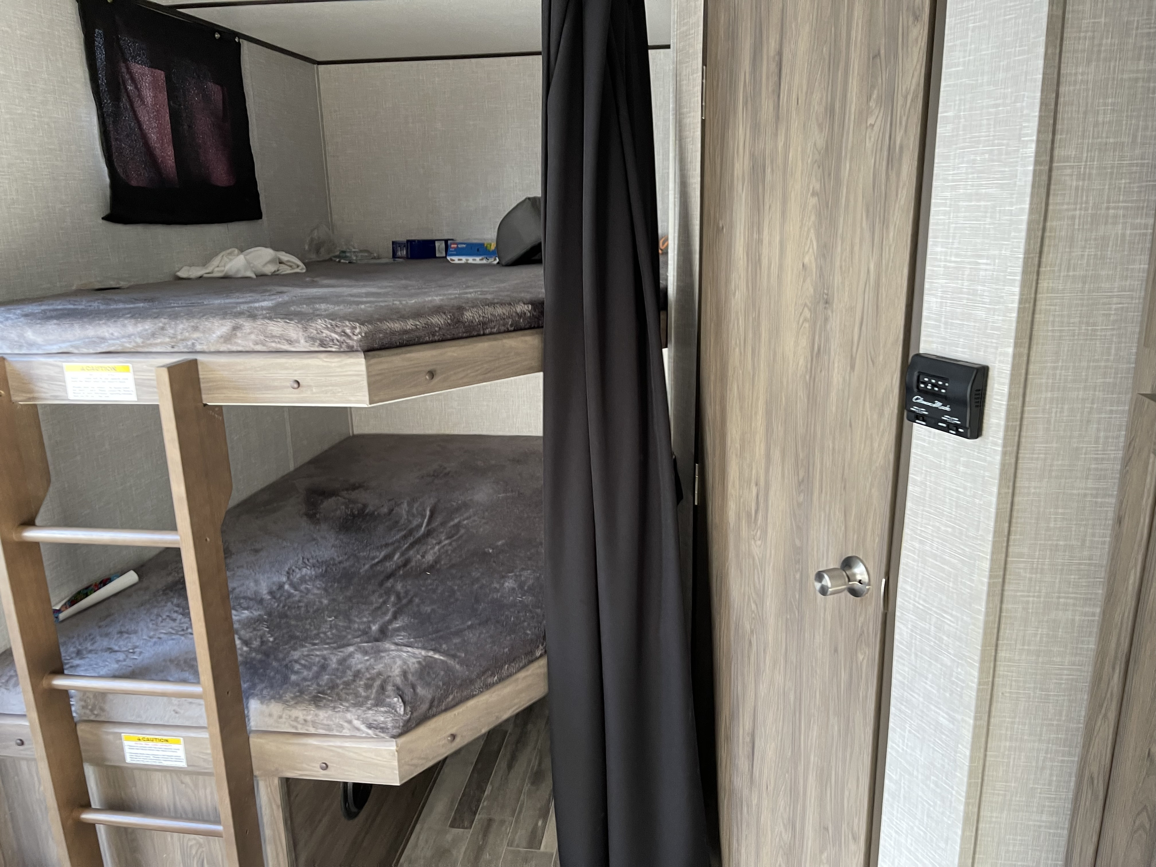 RV rental interior featuring comfortable bunk beds with a ladder, a privacy curtain, and a control panel for cozy travel.. Crossroads RV Zinger Lite 2021