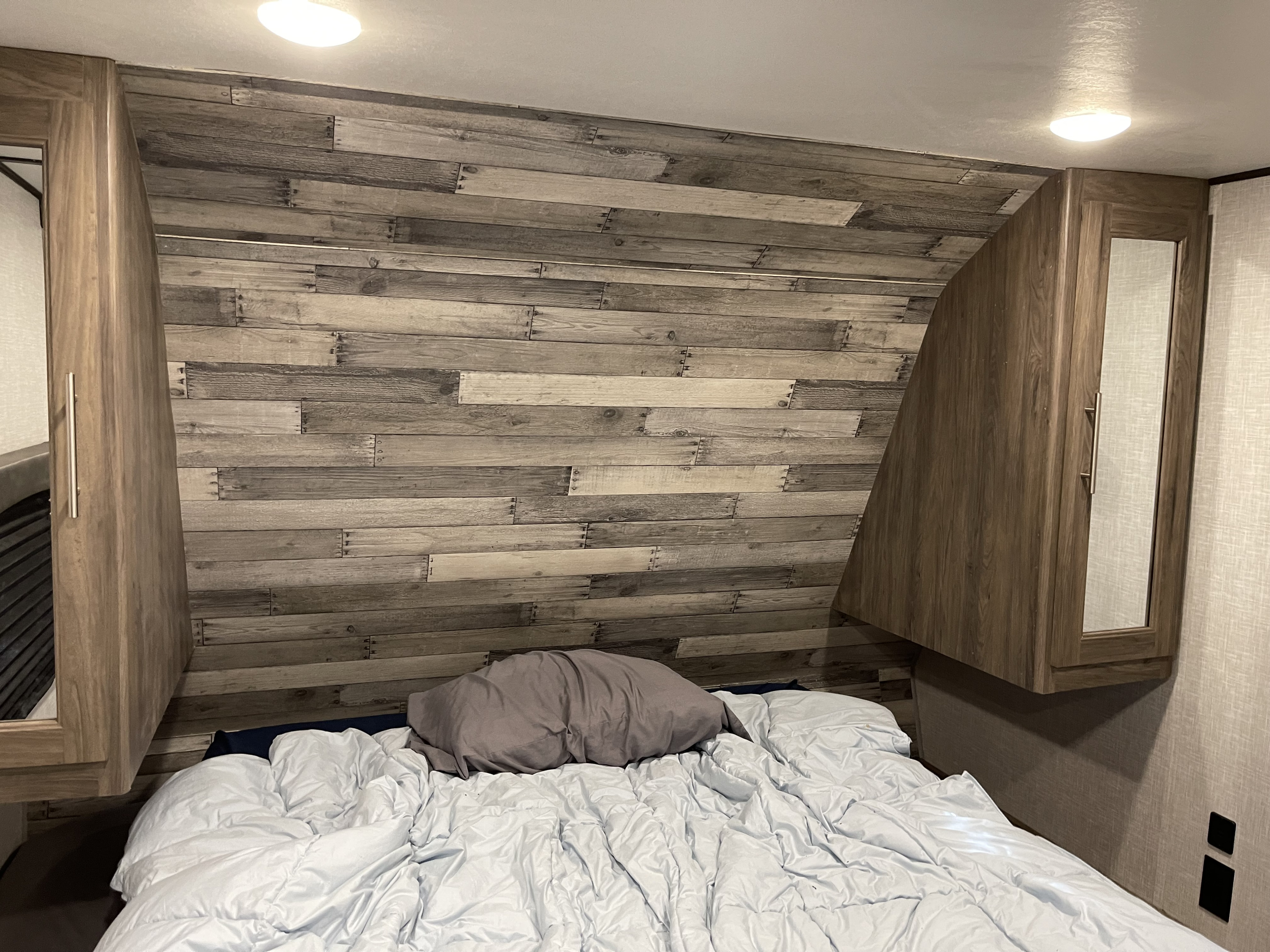 Cozy RV rental bedroom featuring a bed, rustic wood-look wall, and built-in mirrored cabinets on each side.. Crossroads RV Zinger Lite 2021