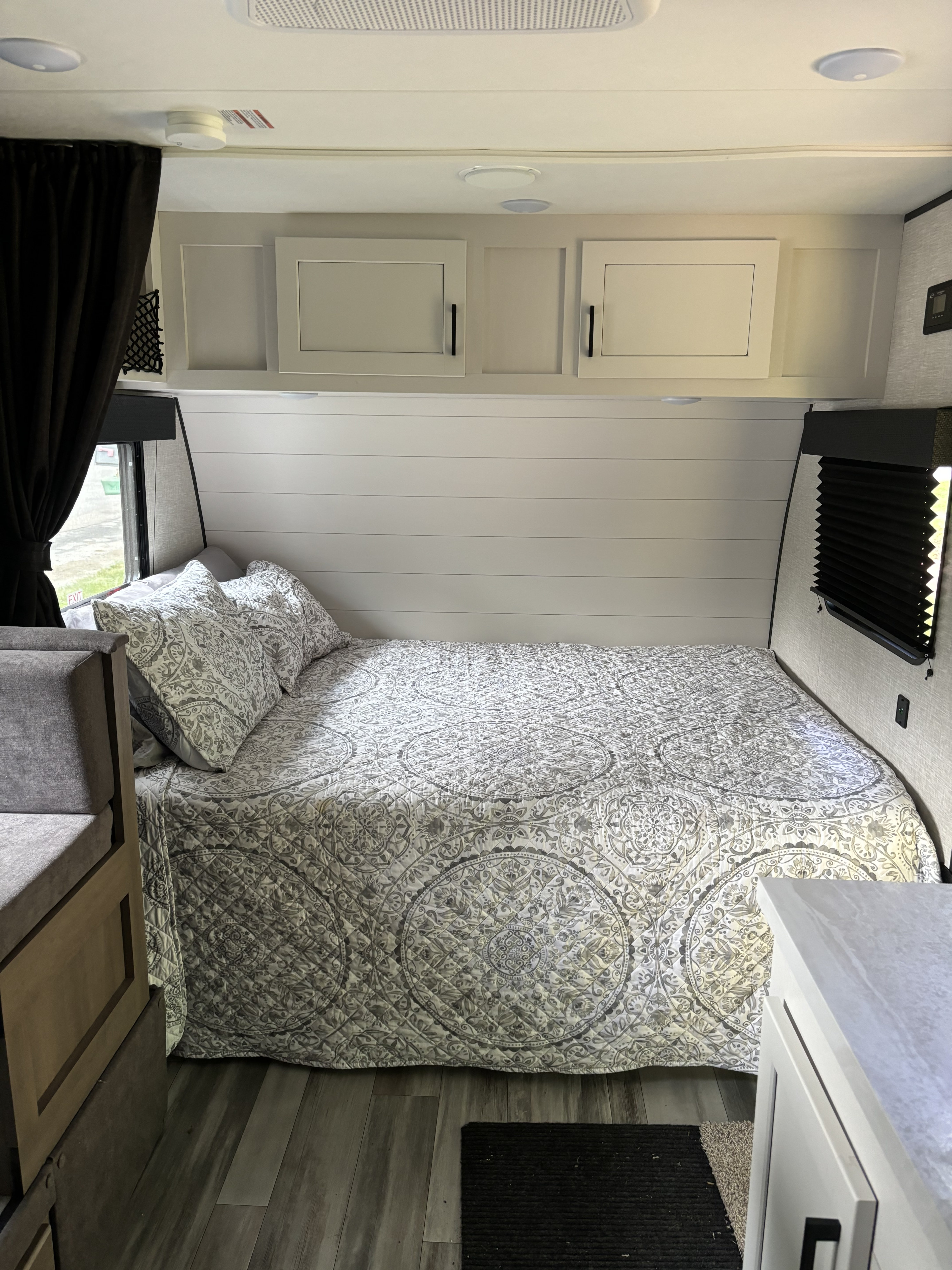 Interior view of an RV rental bedroom with a comfy bed, gray patterned quilt, and shiplap-style walls. Includes overhead storage.. Jayco Jay Flight SLX 2024