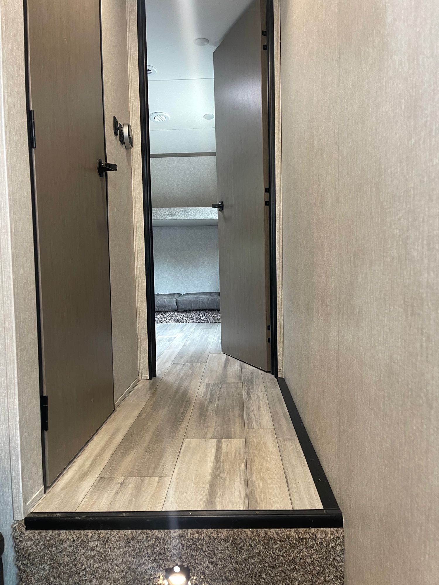 RV rental interior: Hallway with doors leads to bunk beds, featuring wood-look flooring and a step down.. Forest River Coachmen Chaparral Lite 2022