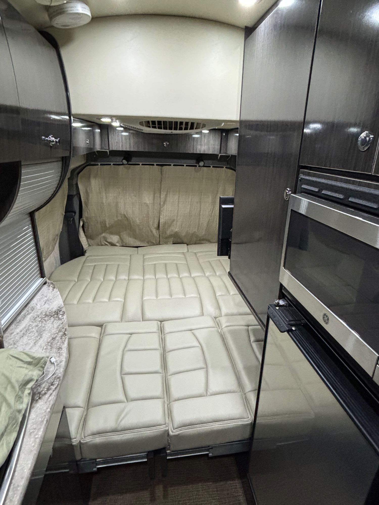 Inside a modern RV rental: a plush modular bed, sleek dark cabinets, built-in microwave, and fridge. Ready for travel comfort.. Airstream Avenue 2012
