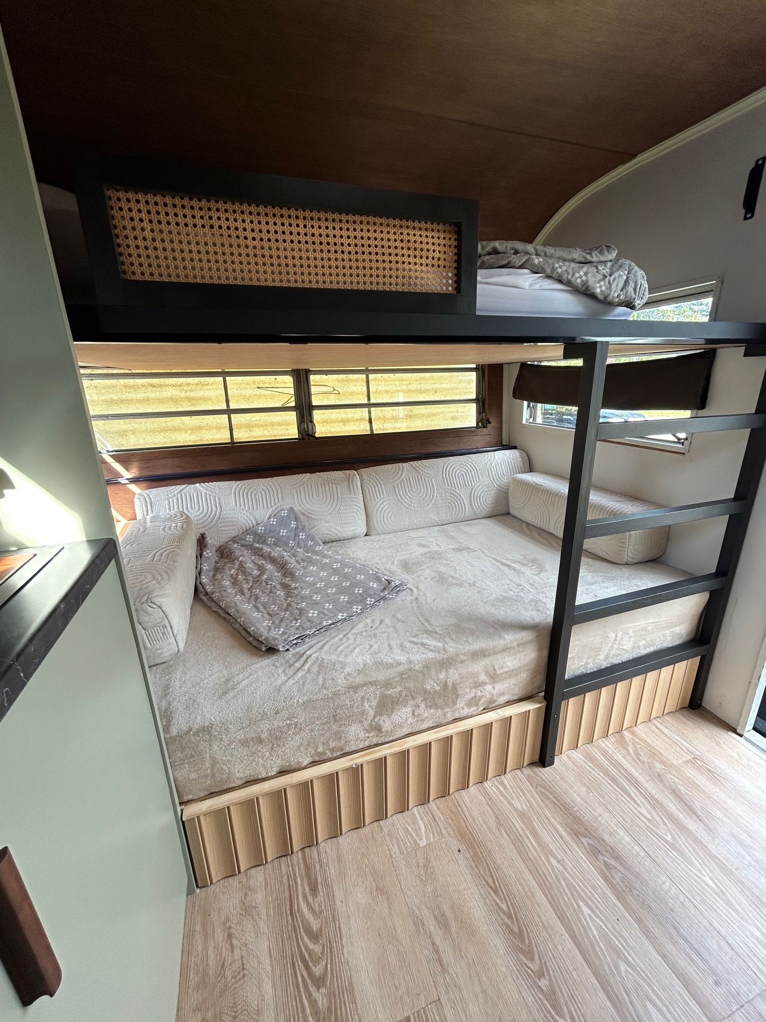 Cozy RV rental interior featuring a bunk bed setup with a lower sofa bed, upper rattan-paneled bunk, and wood accents. Perfect for mobile living.. Glendale Golden Falcon 1967