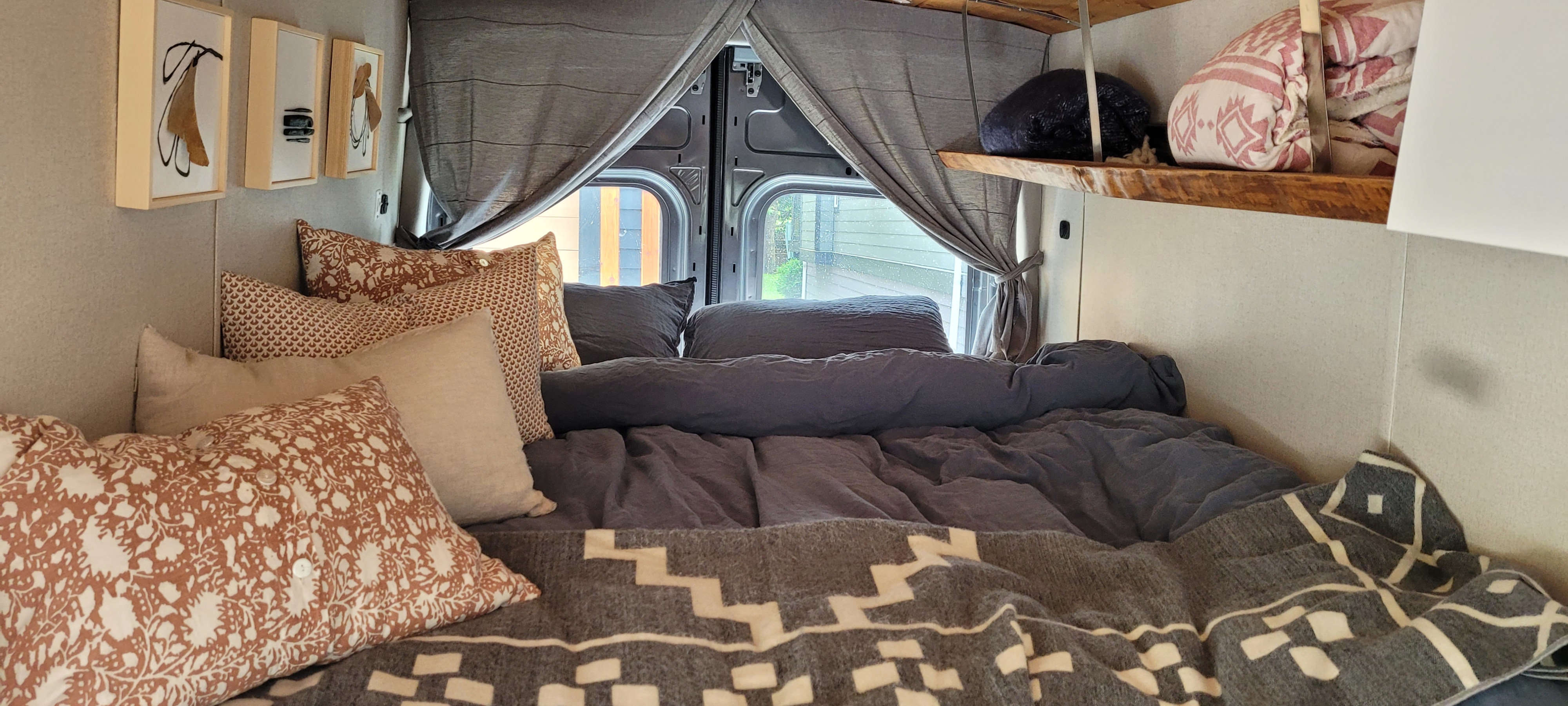Cozy RV rental bedroom with patterned pillows, soft bedding, and artistic decor. Perfect for a comfortable road trip.. Ford Transit 2020