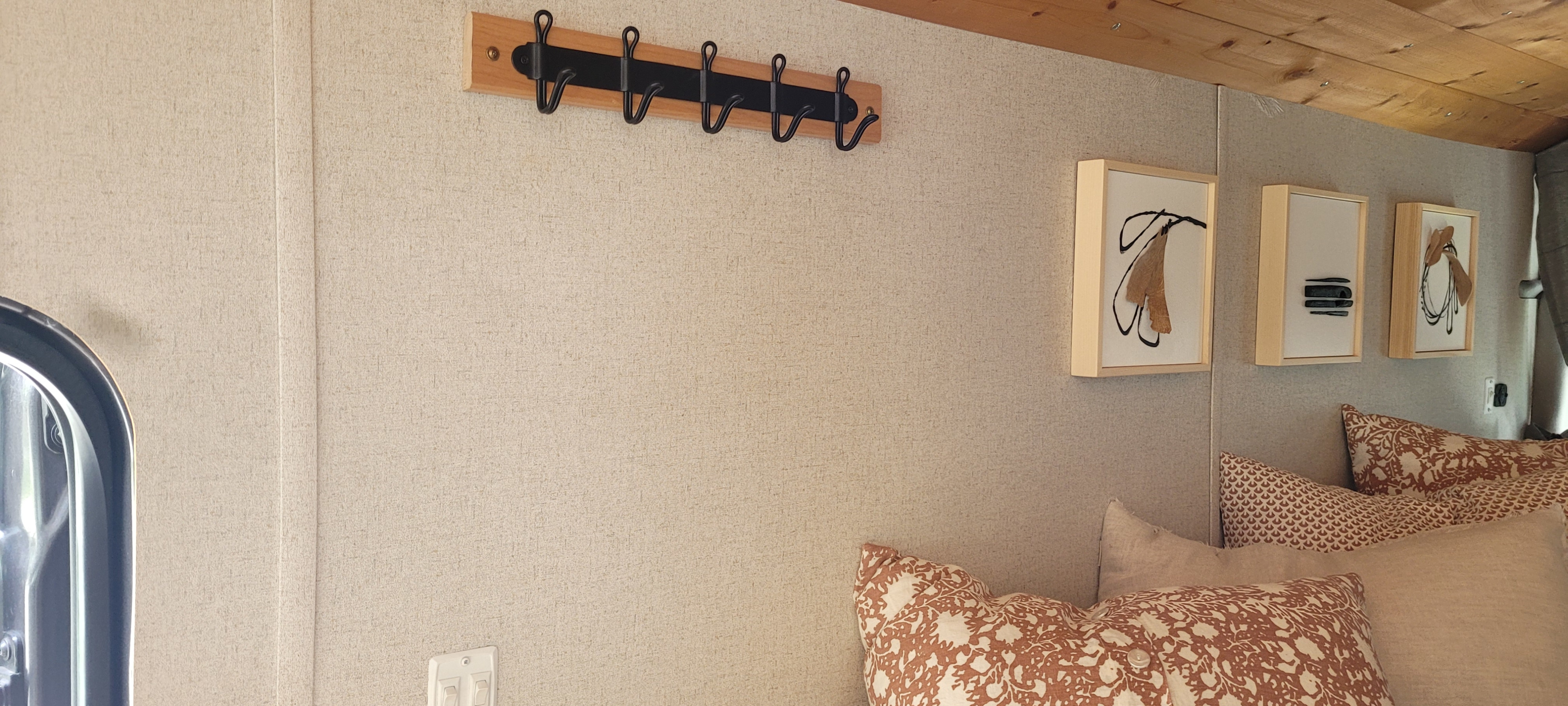 RV rental interior with light walls, wooden ceiling, coat rack, modern art, and patterned pillows for a cozy, stylish stay.. Ford Transit 2020