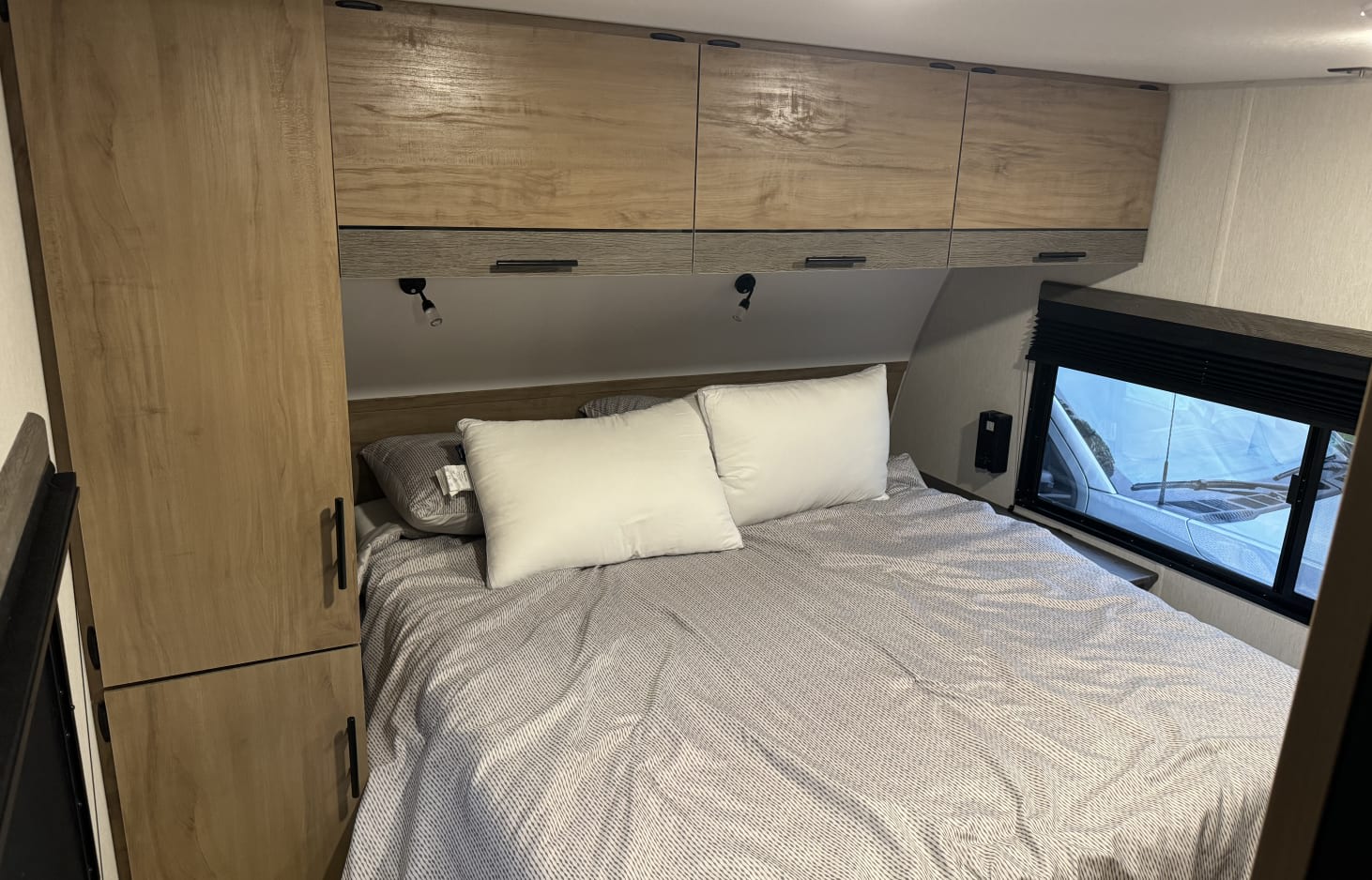 This RV rental bedroom has a bed with pillows, wooden cabinets, and a wardrobe for your travels.. Forest River Campsite Reserve 26CJ 2024